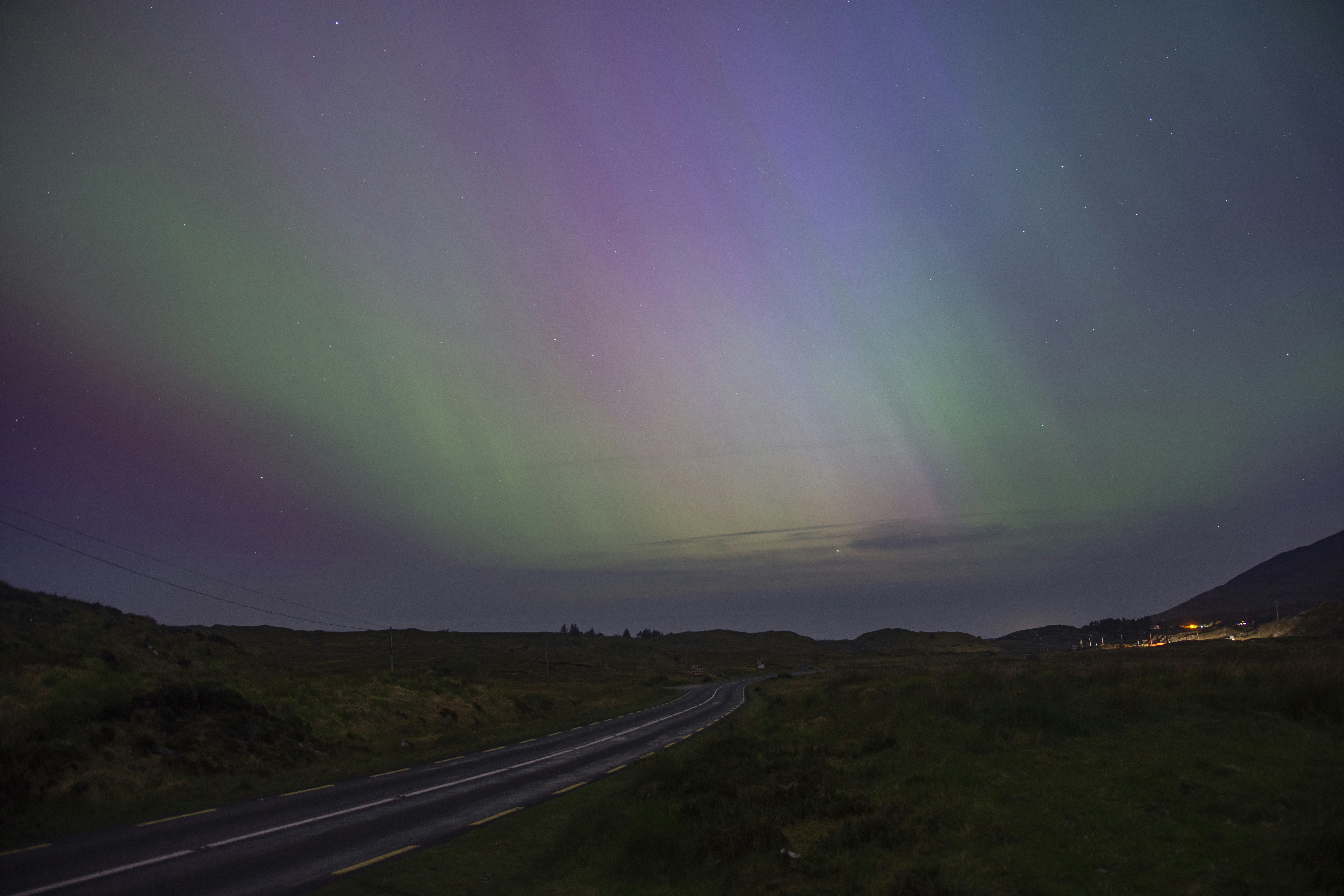 Aurora borealis lights up the night sky over a road.