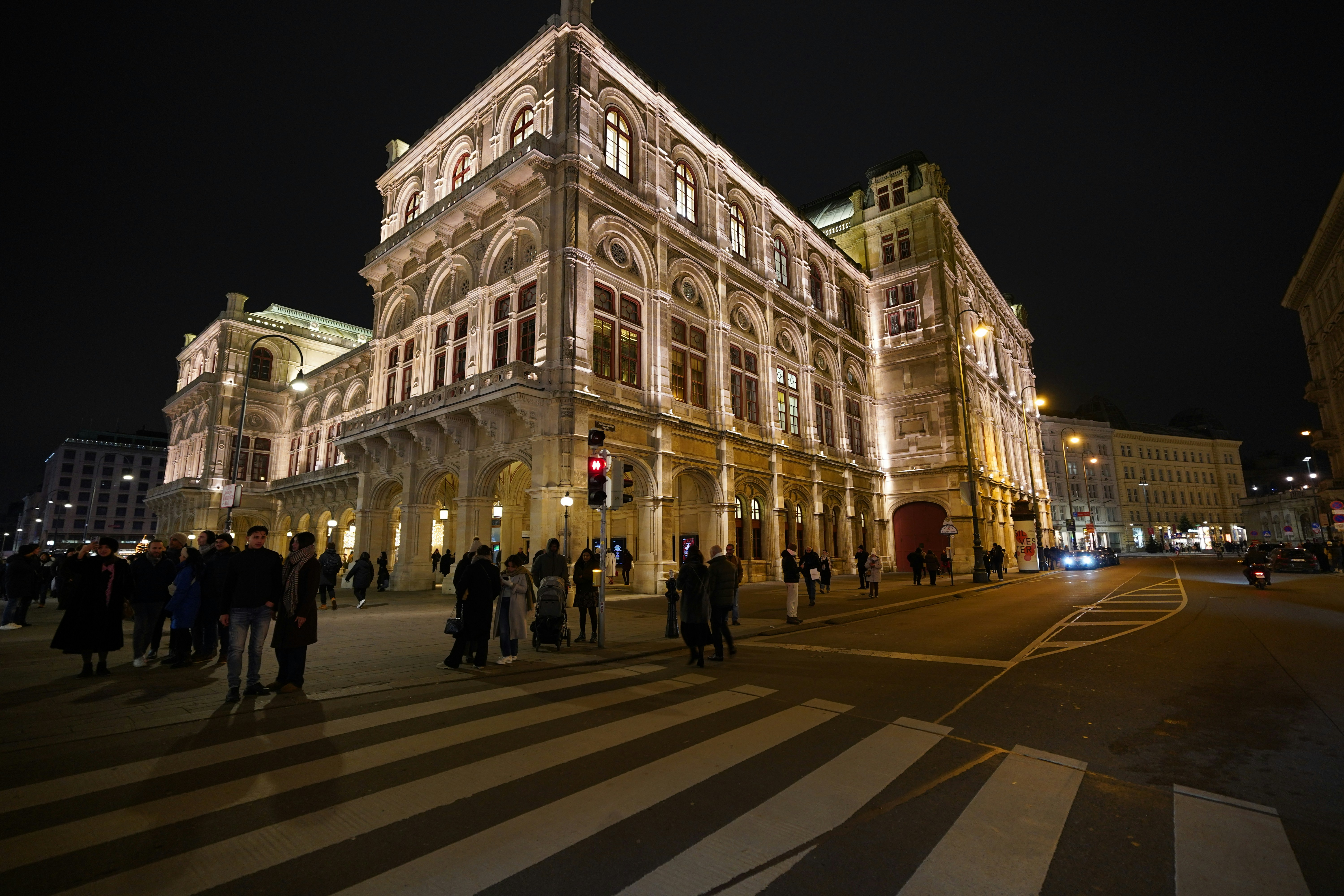 Ornate building illuminated at night with people crossing street