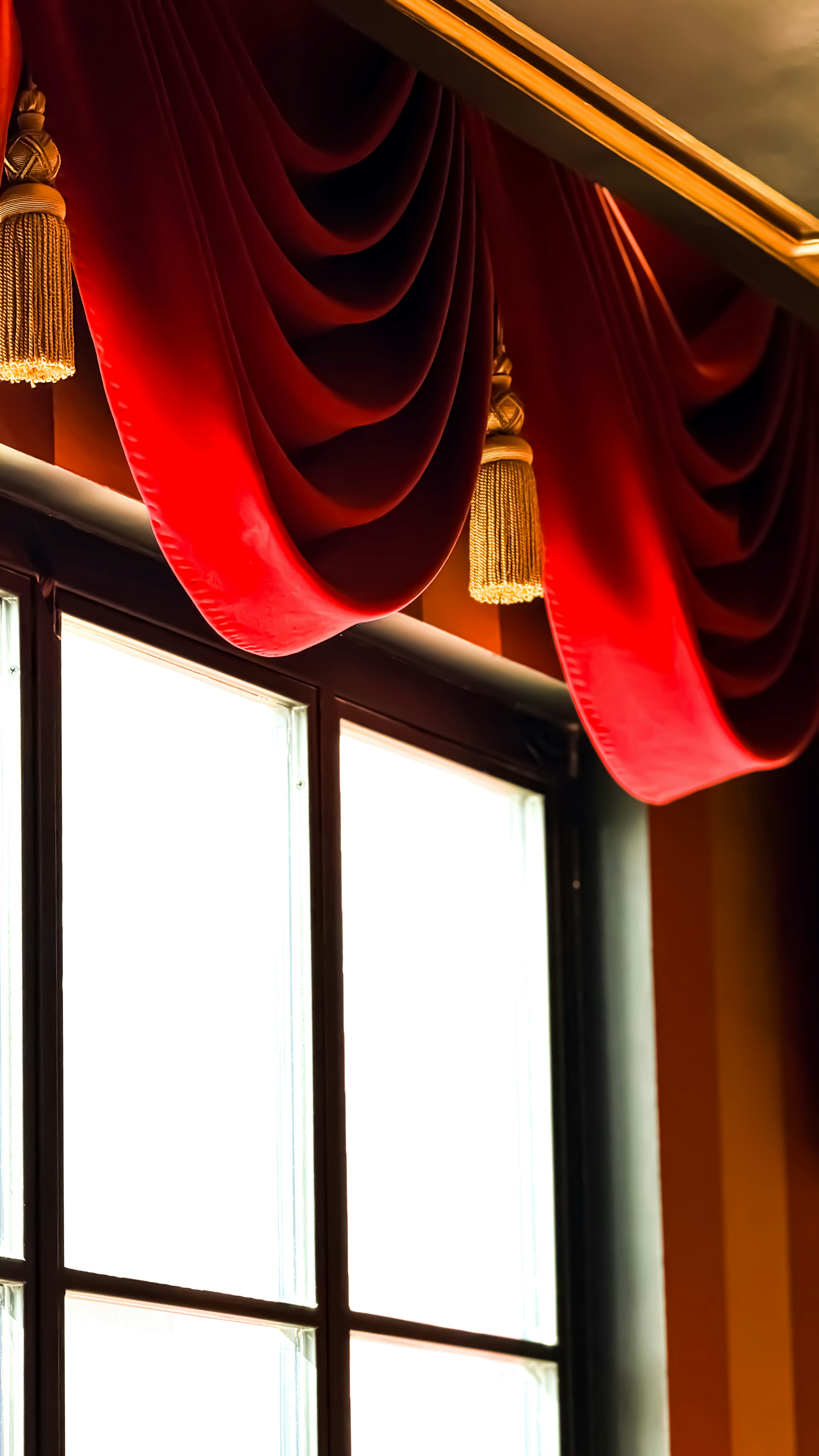 Red velvet drapes with gold tassels hang over window