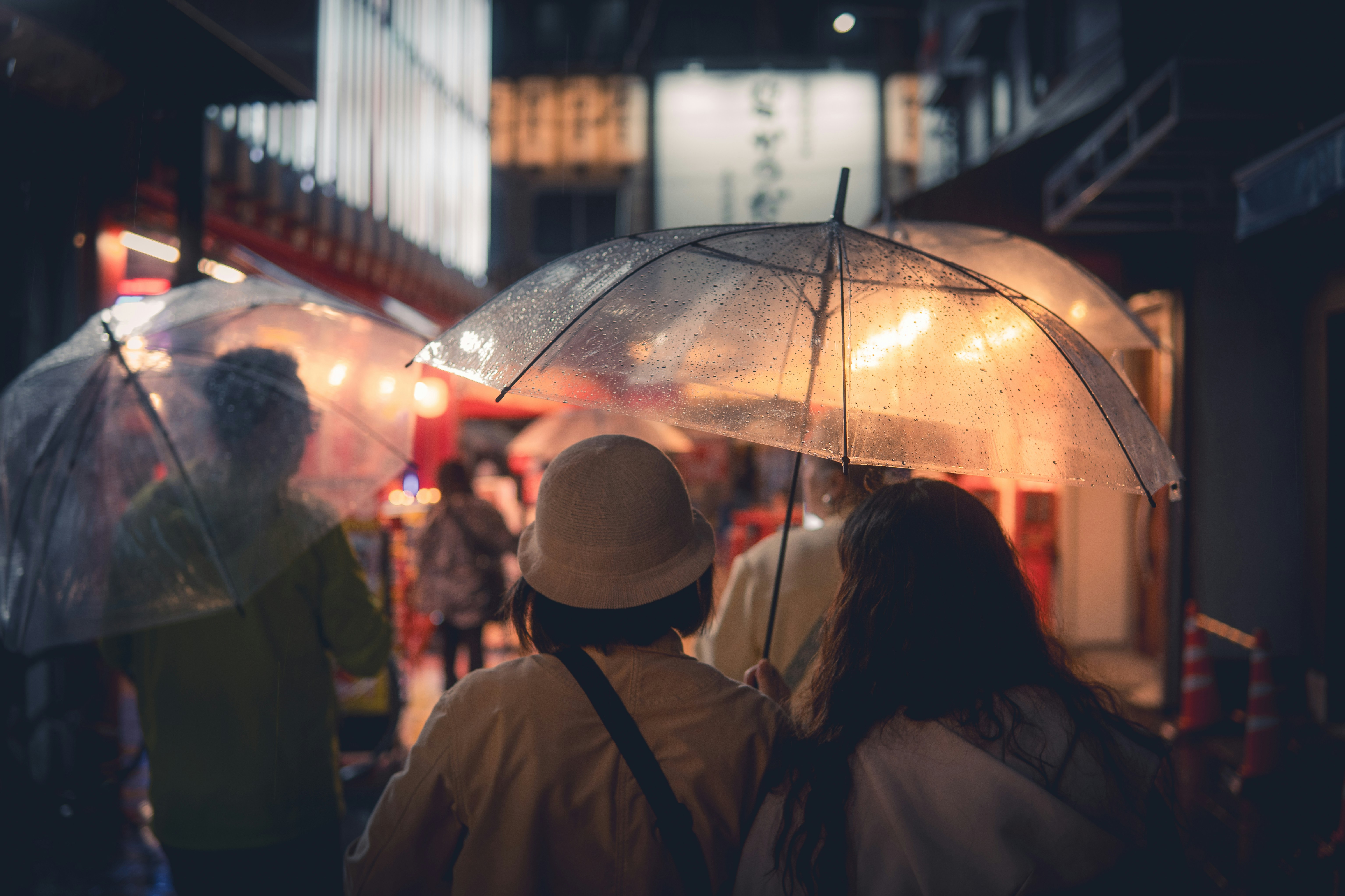 People walk with umbrellas down a dimly lit street.