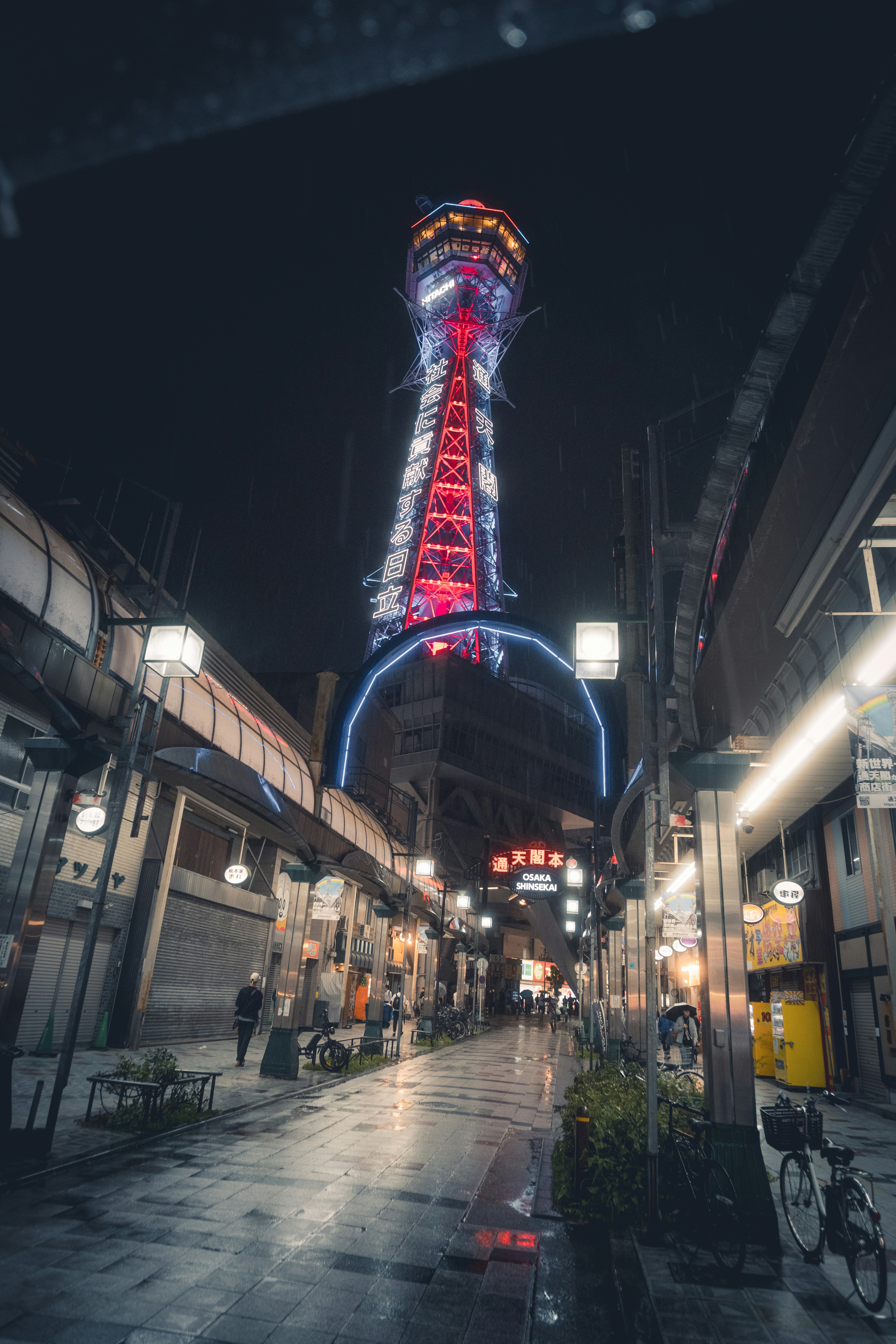 Uma torre alta iluminada à noite acima de uma rua.