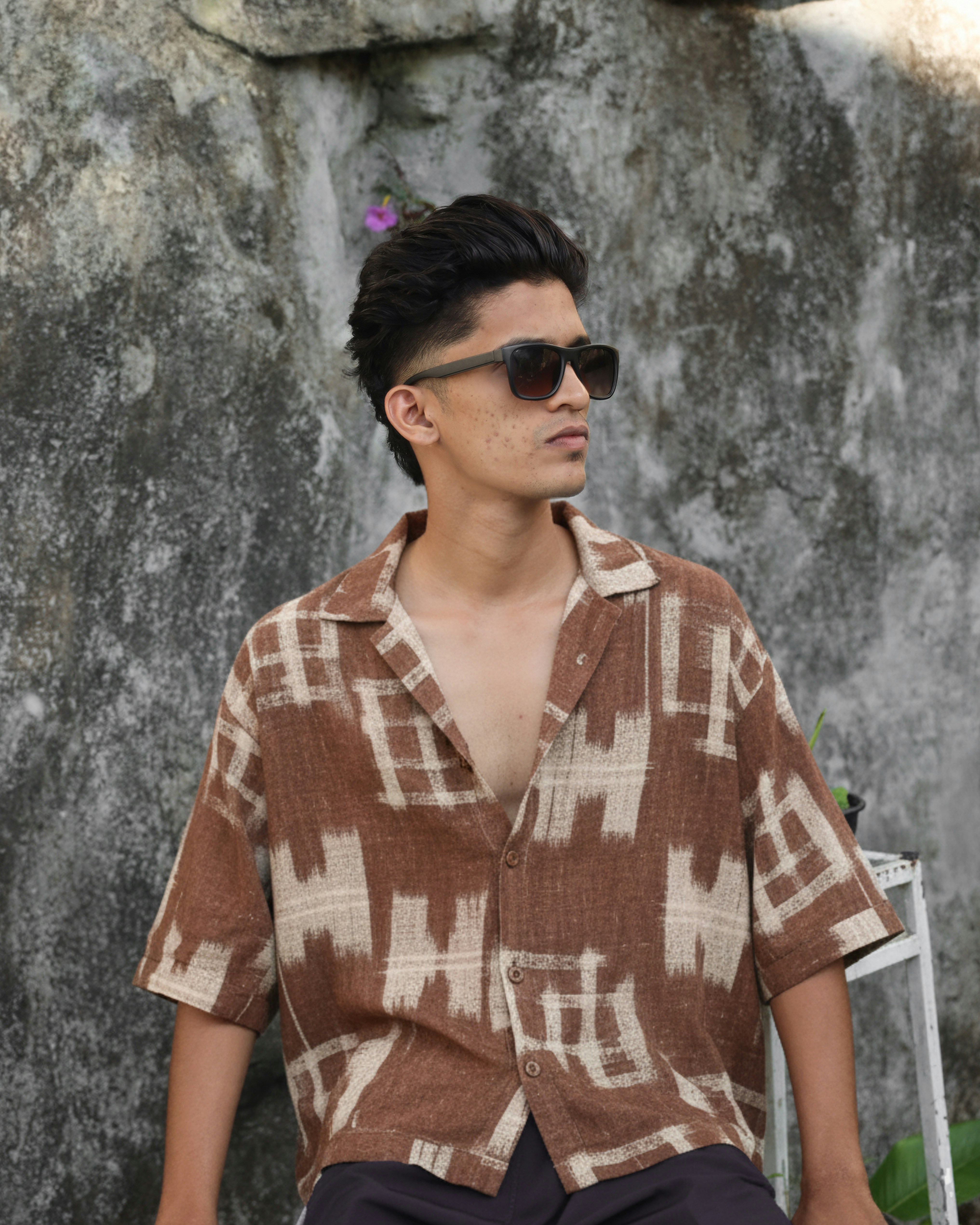 Young man wearing sunglasses and patterned shirt outdoors.