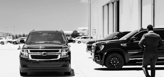 Man in suit walks past black suvs in parking lot.