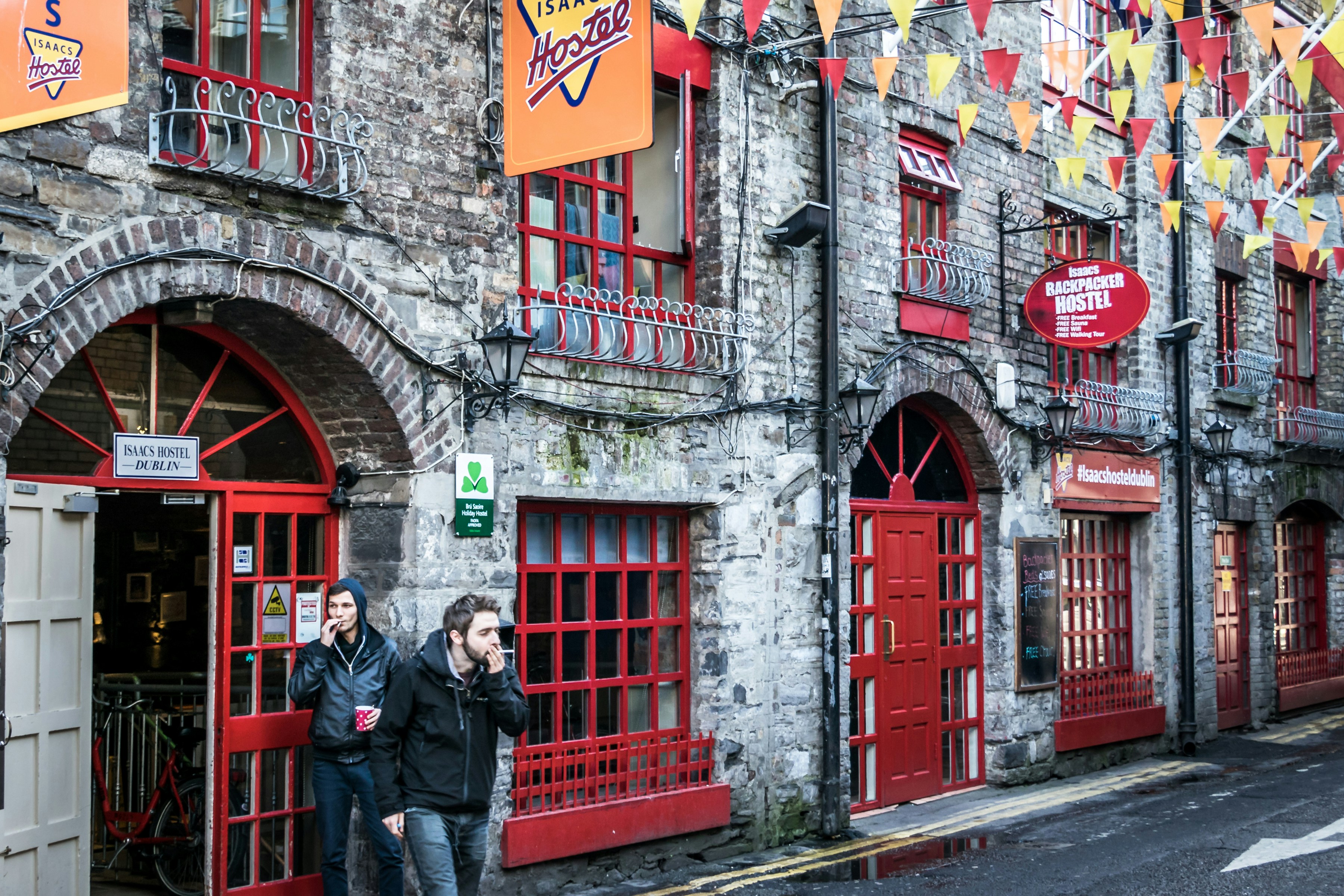 People walk past old brick buildings with red doors