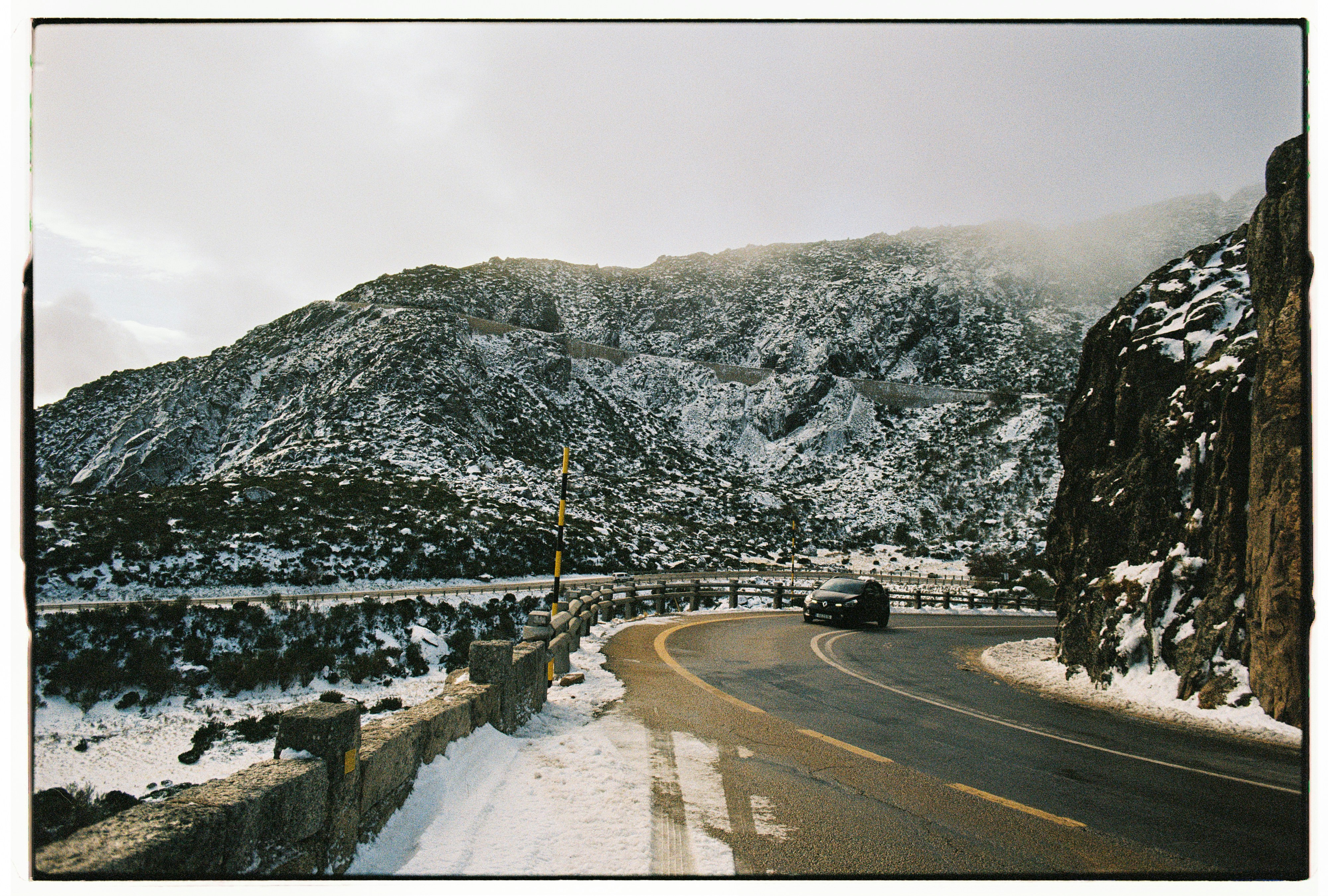 A car drives on a winding mountain road in winter.