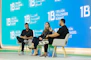 Three people sit on chairs on a stage discussing.