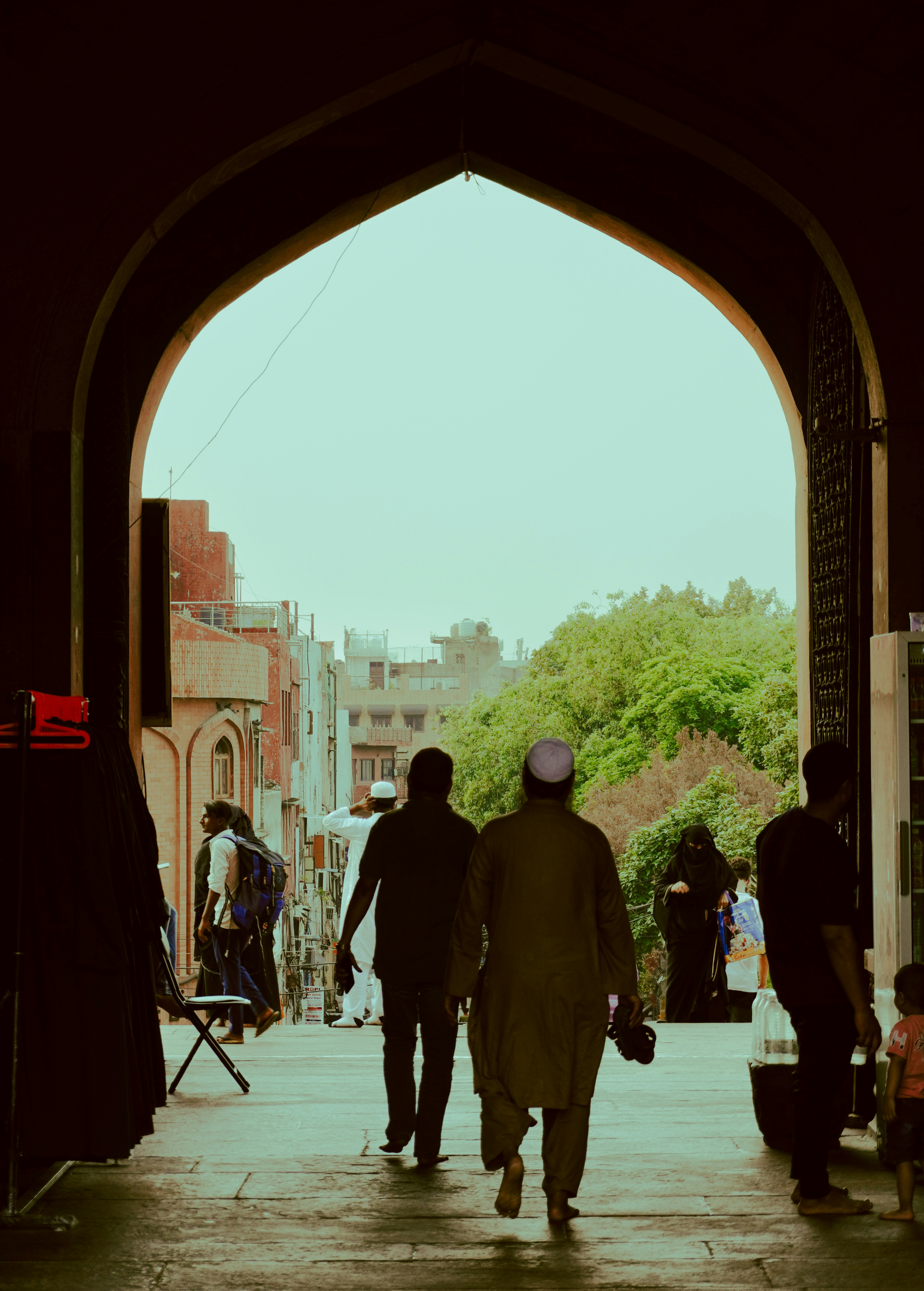 People walk through an arched entryway into a bustling street.