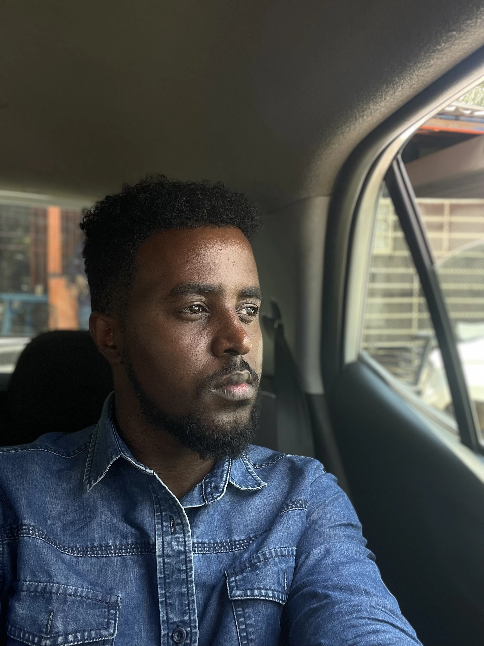 Man in denim shirt looking out car window