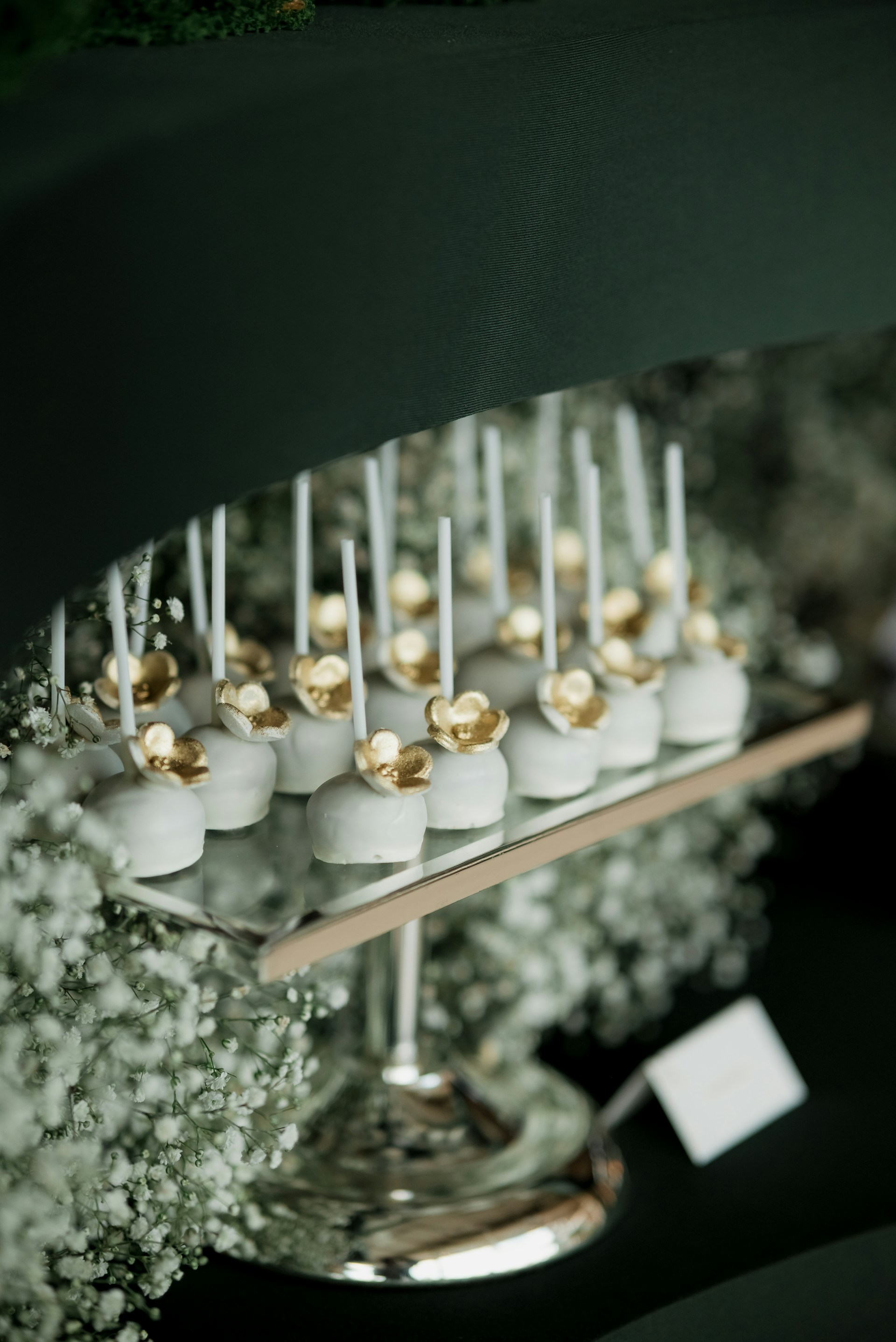 White cake pops with gold flower decorations on a platter.