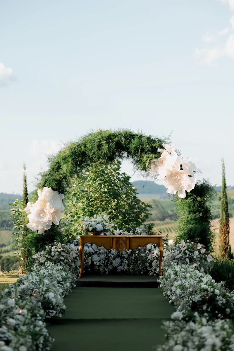 A wedding arch of greenery and white roses against the hills