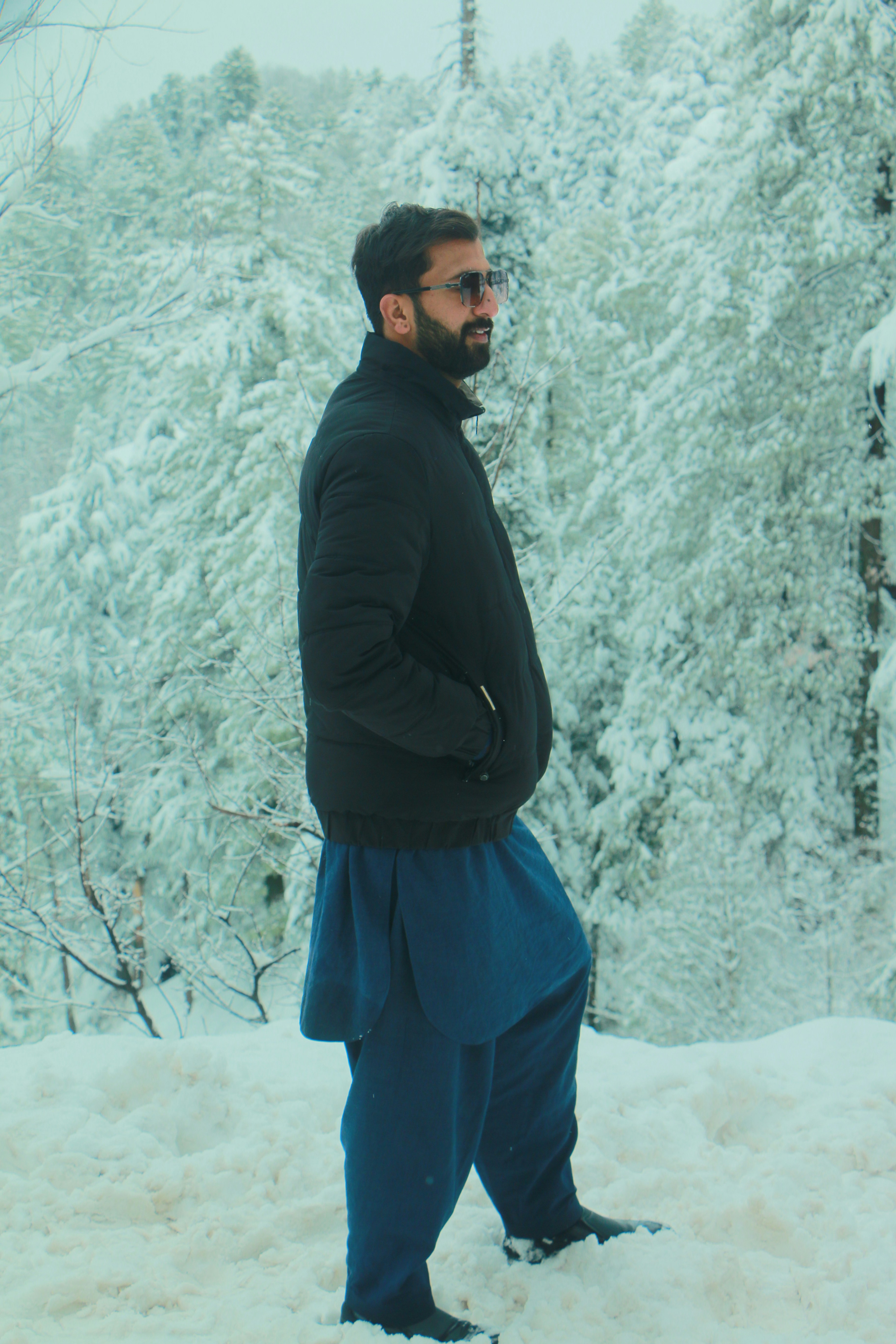 Man in winter clothing stands in snow-covered forest.