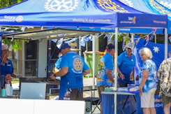 People gathered under blue rotary tents at an outdoor event.