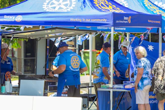 People gathered under blue rotary tents at an outdoor event.
