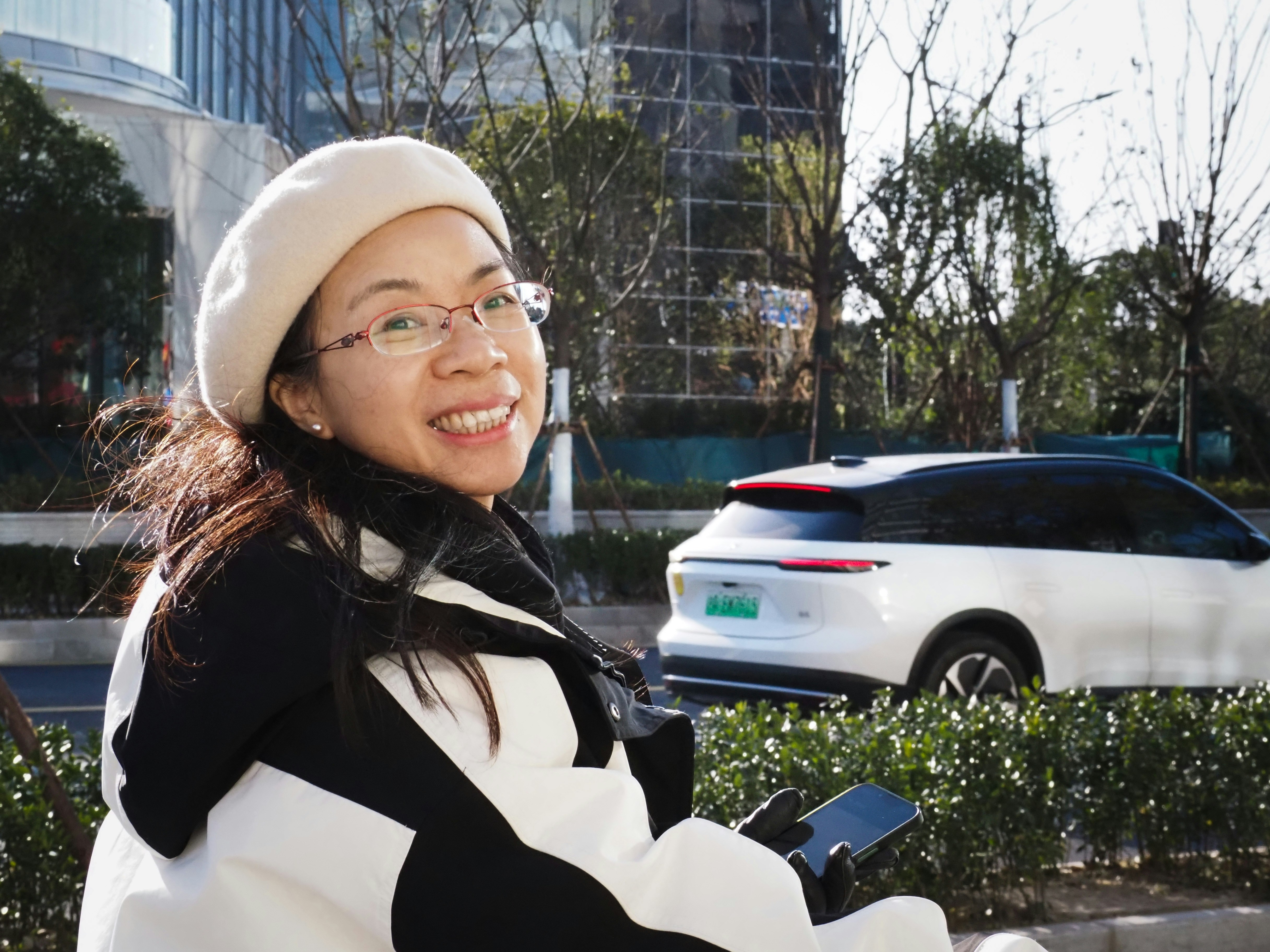 A woman wearing a beret and glasses smiles outside.