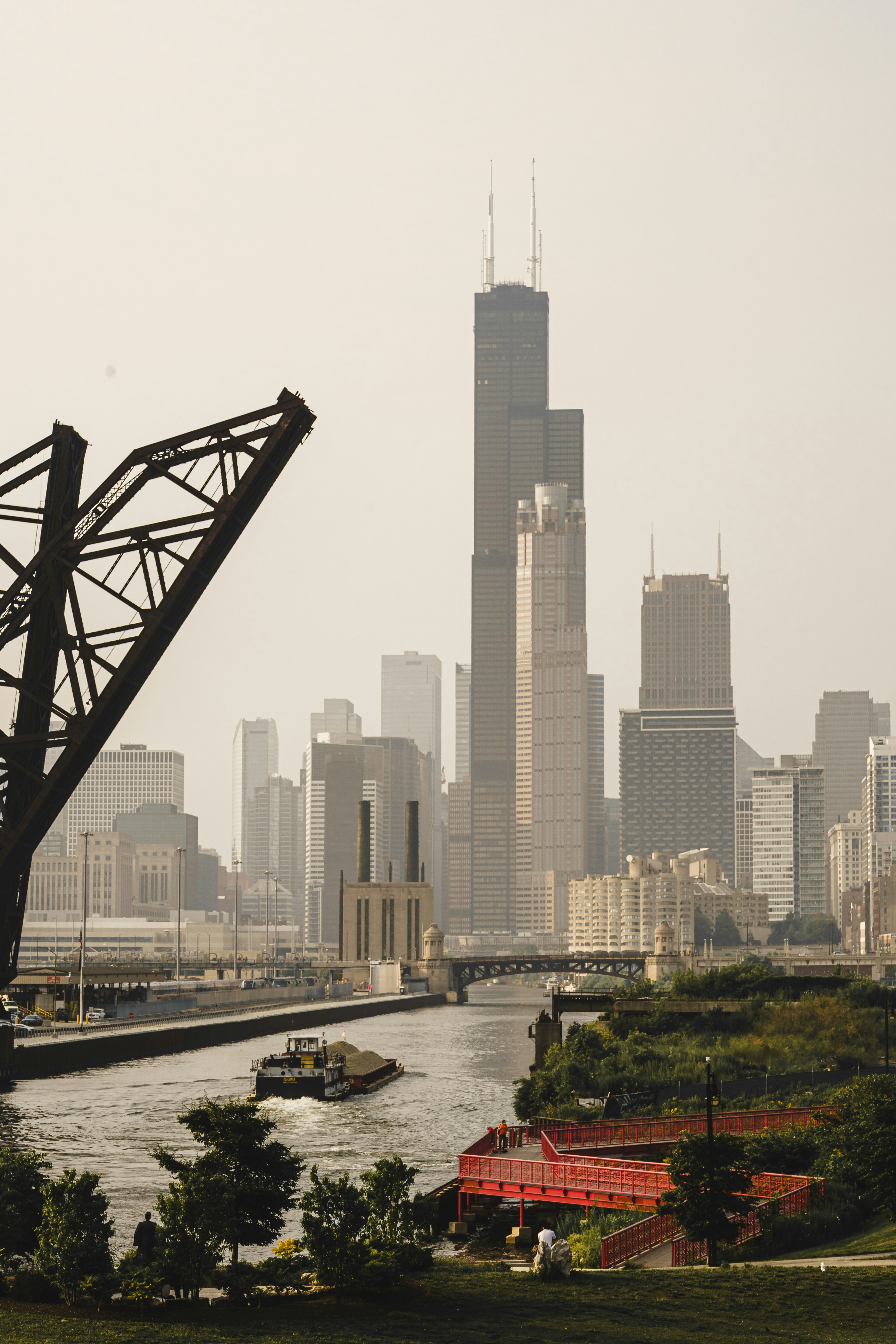 Skyscrapers rise above a river with a barge.