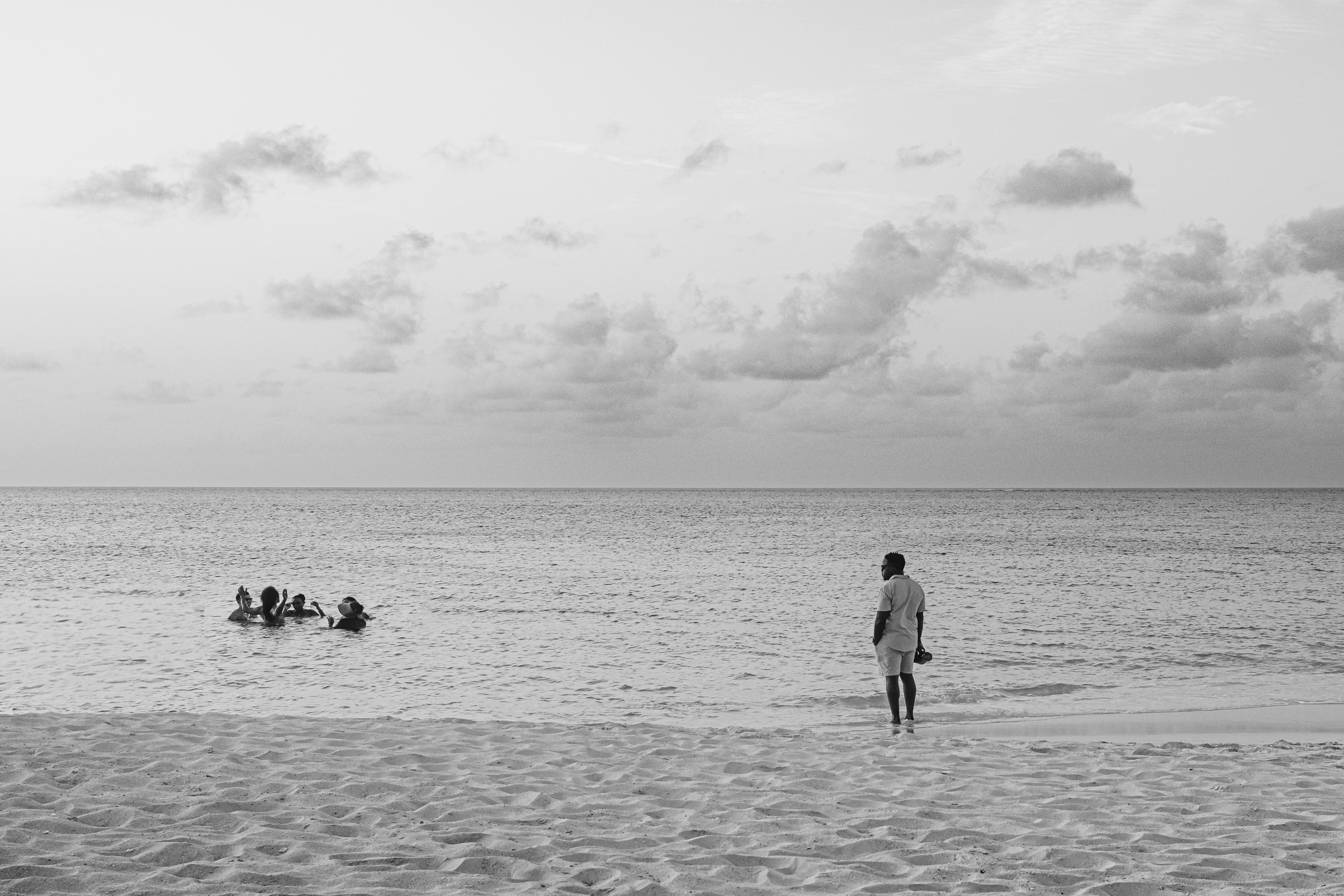 Man stands on beach watching people in ocean