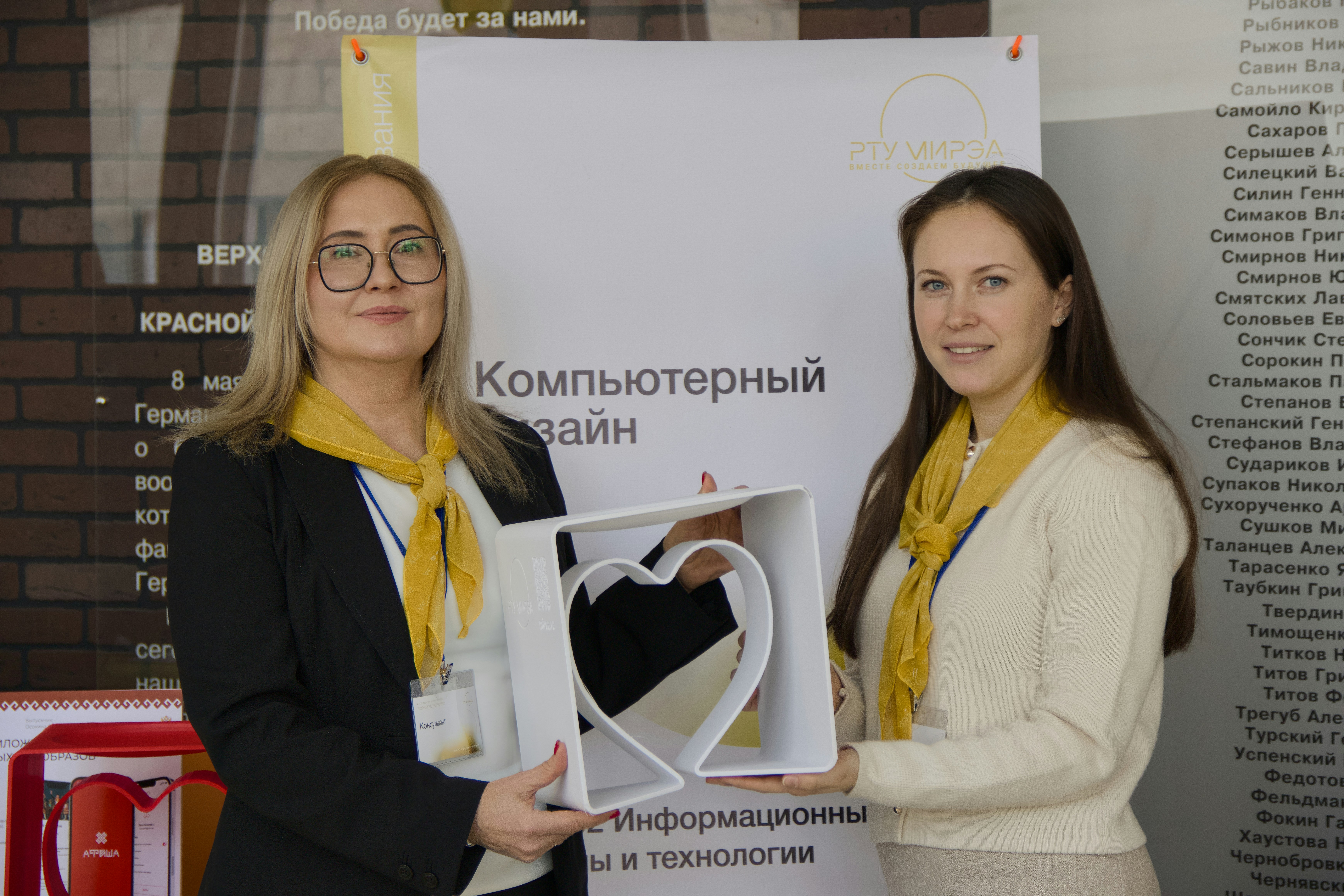 Two women hold a white heart-shaped frame.