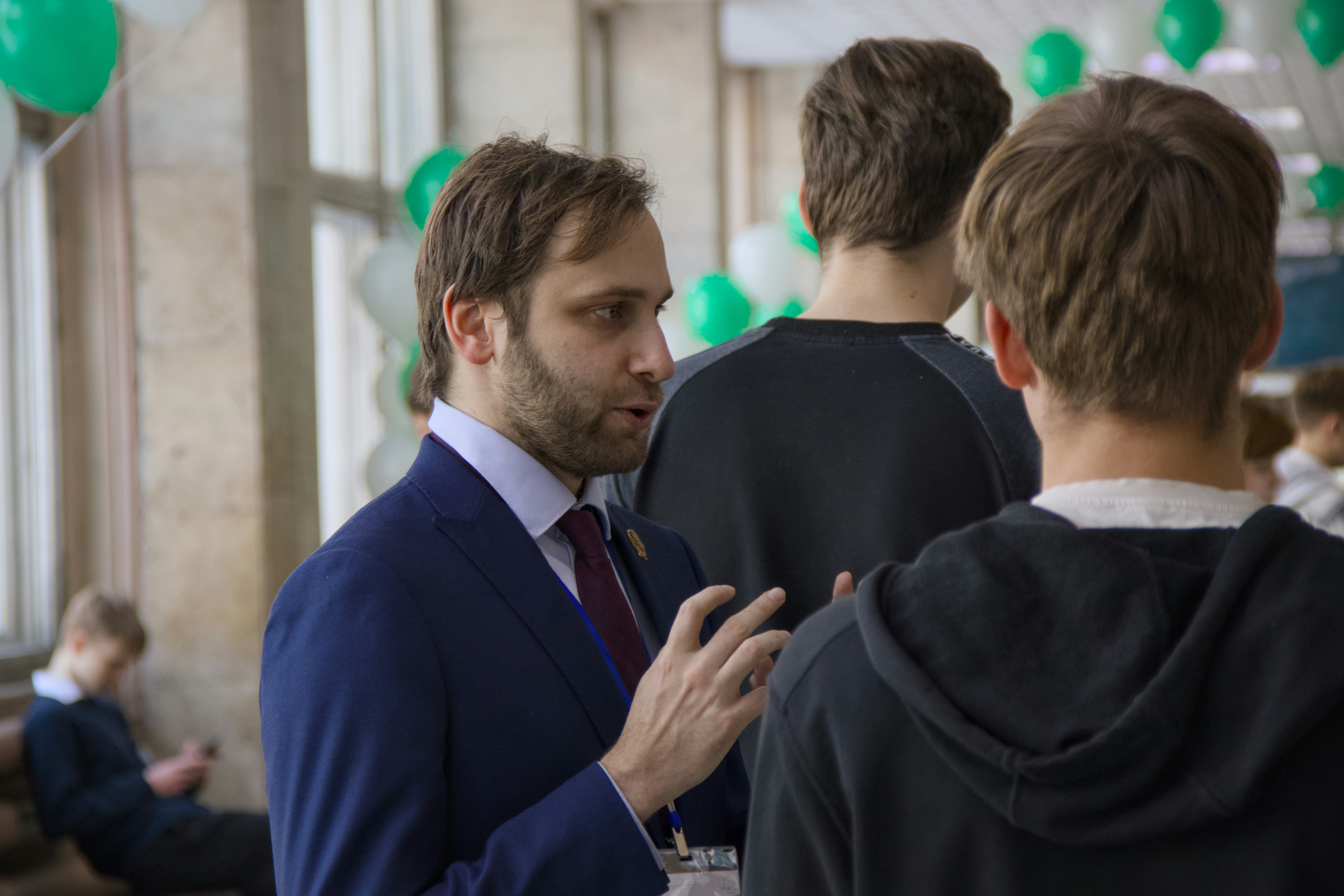 A man in a suit talks to two young men.