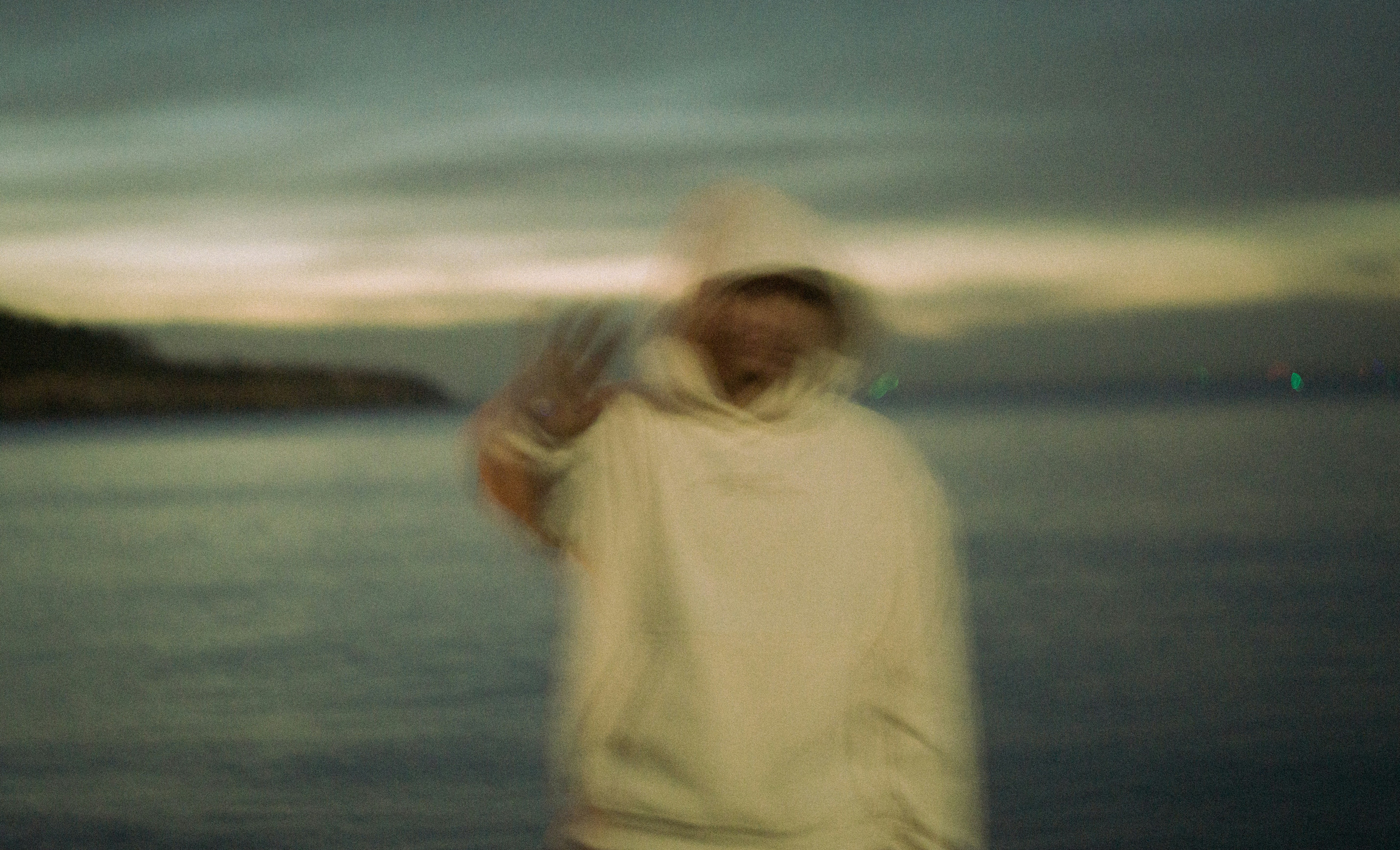 Person in a white hoodie waving by the ocean
