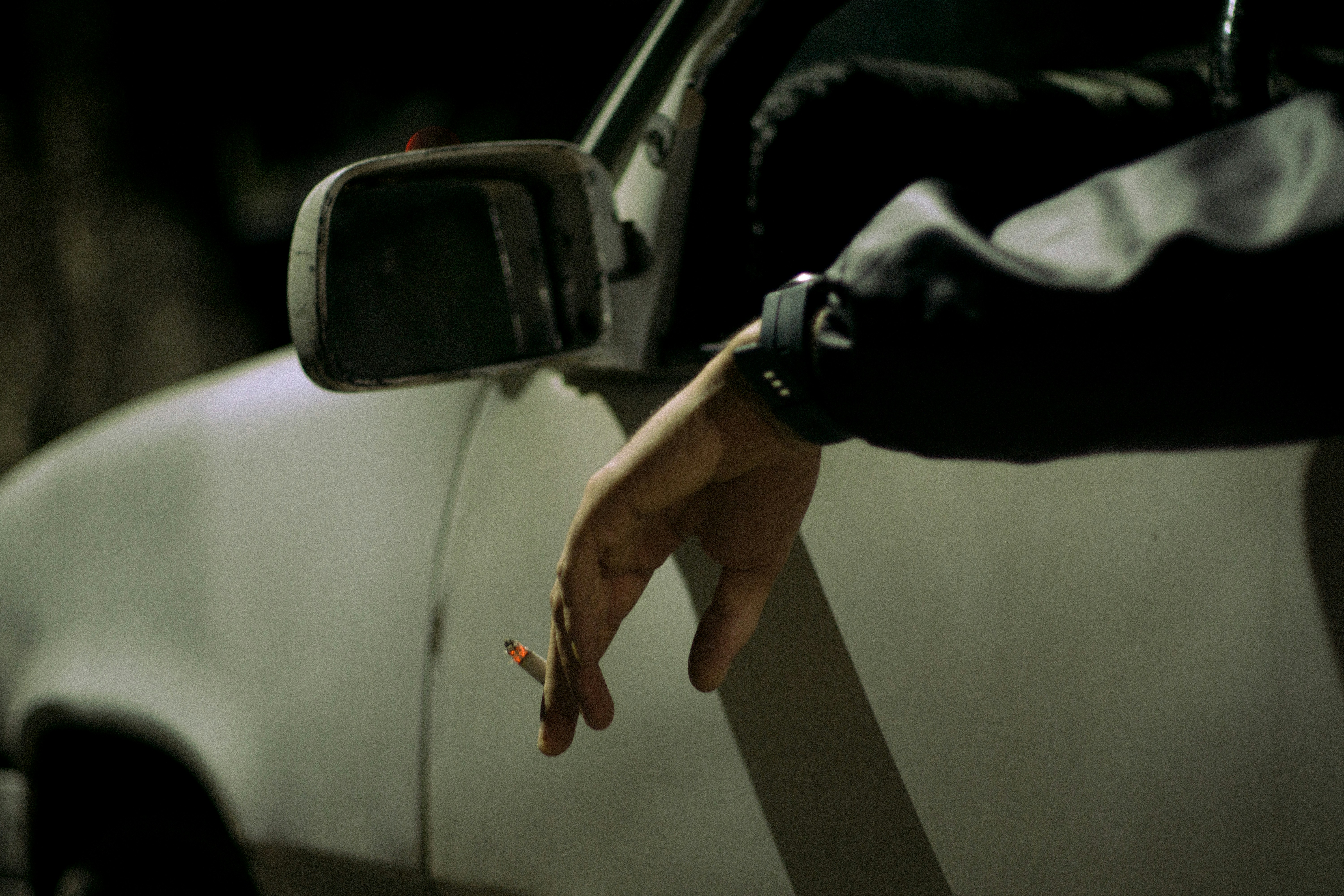 Person's hand holding cigarette out car window
