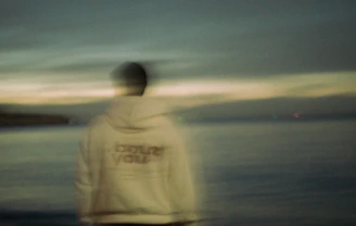 Person in hoodie looking out at the ocean.