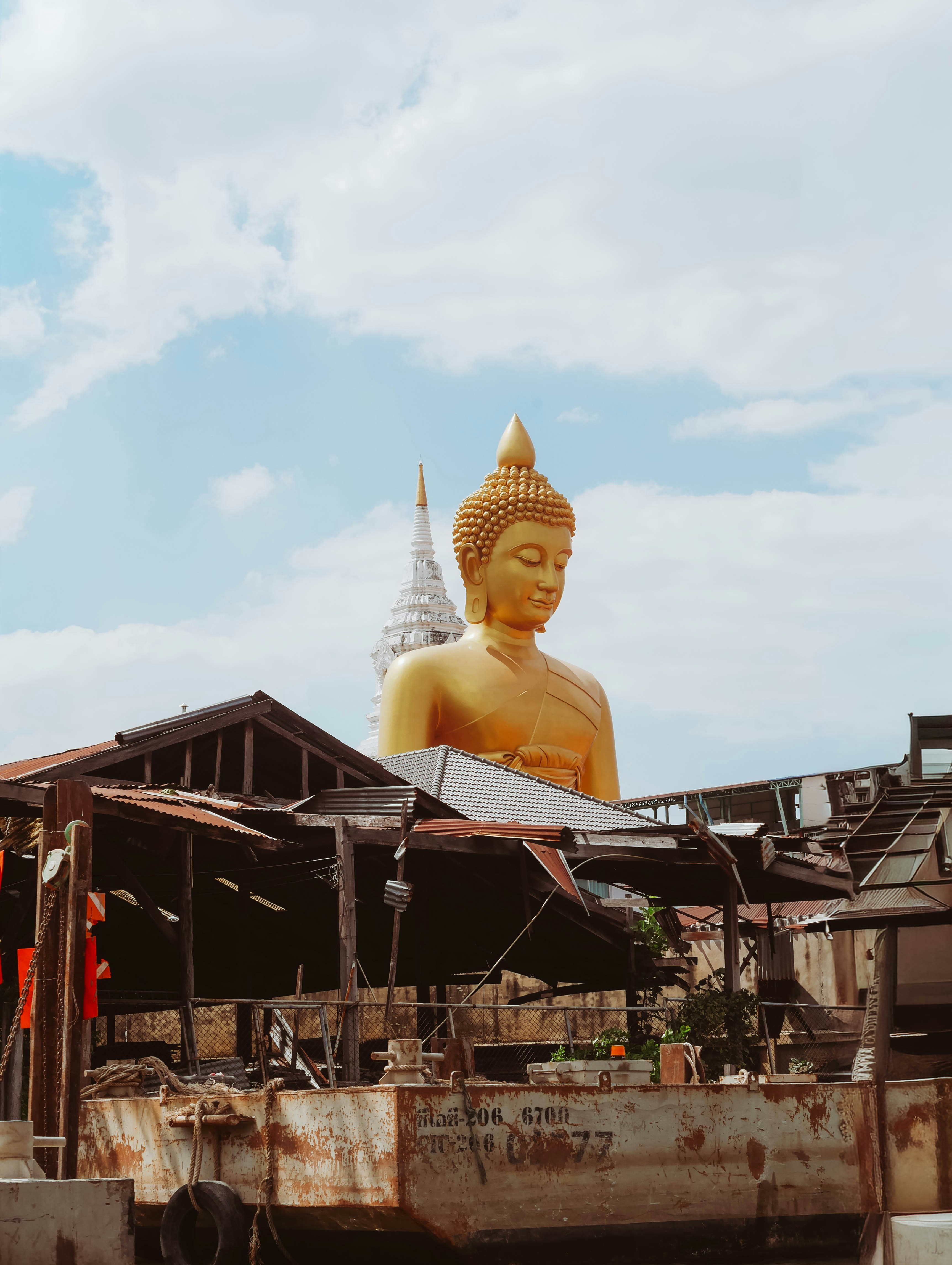 Golden buddha statue towering over rustic buildings.