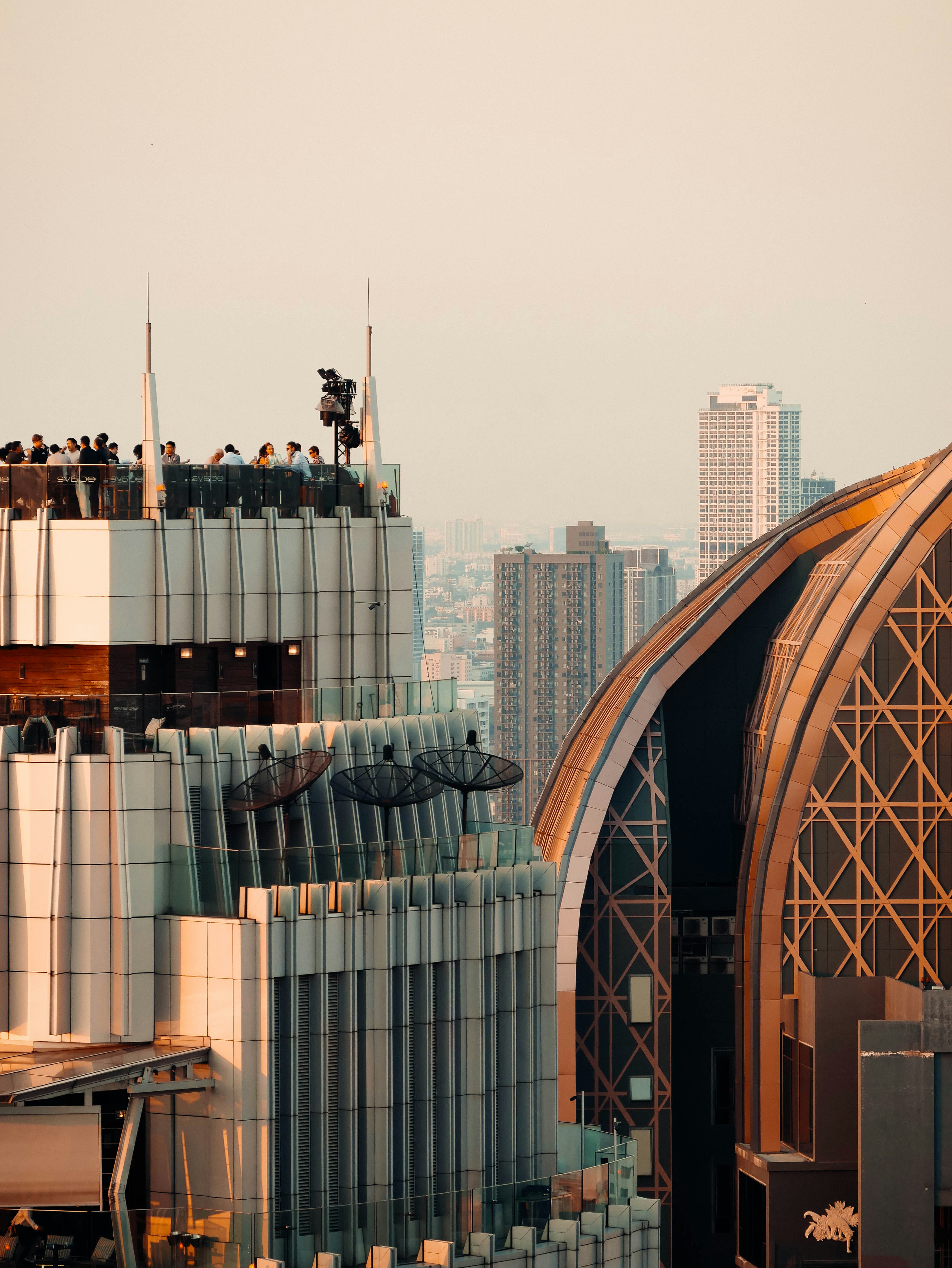 Modern skyscrapers with people on rooftop deck at sunset