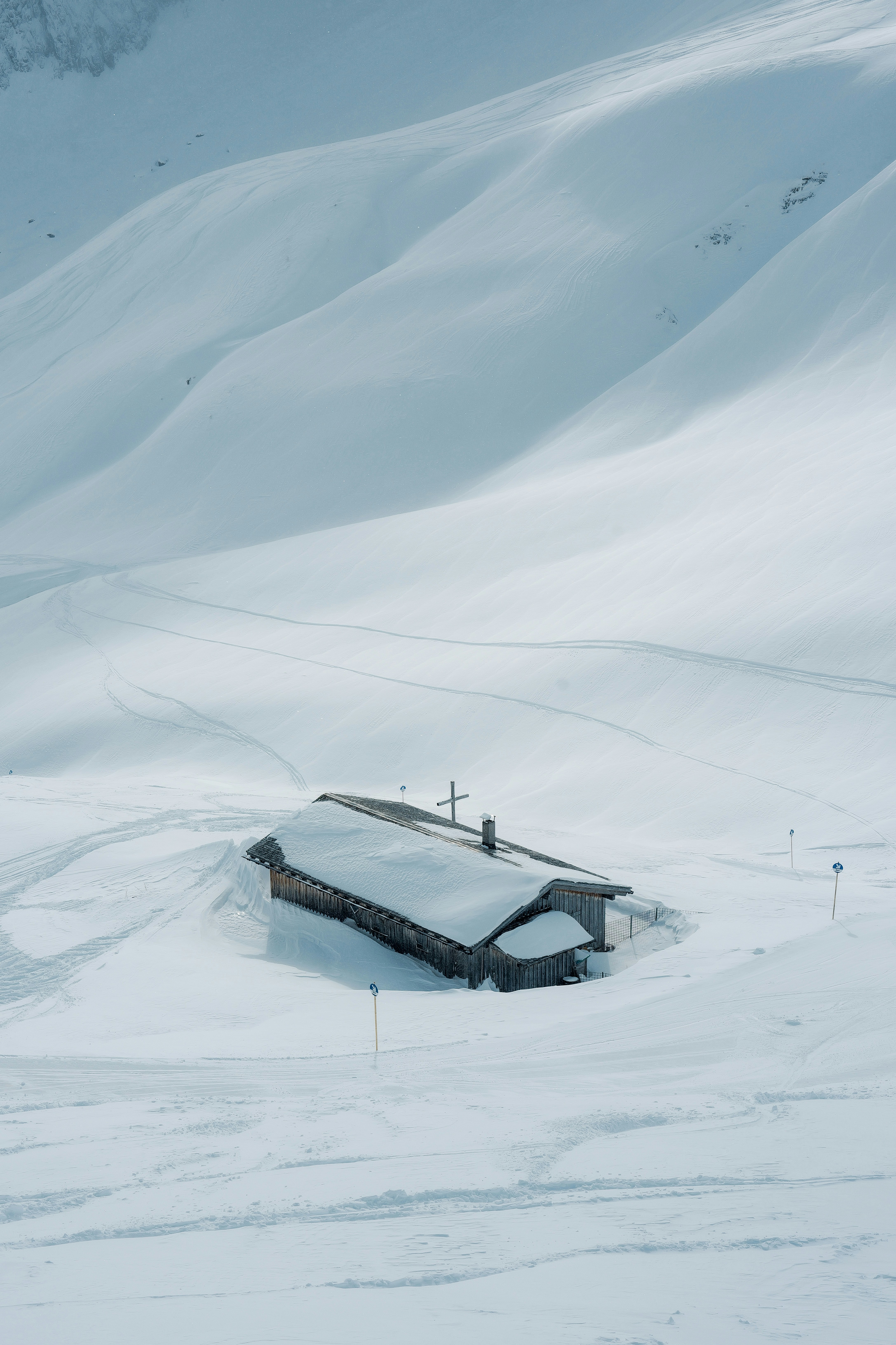 Snow covered cabin in a vast, white mountain landscape.