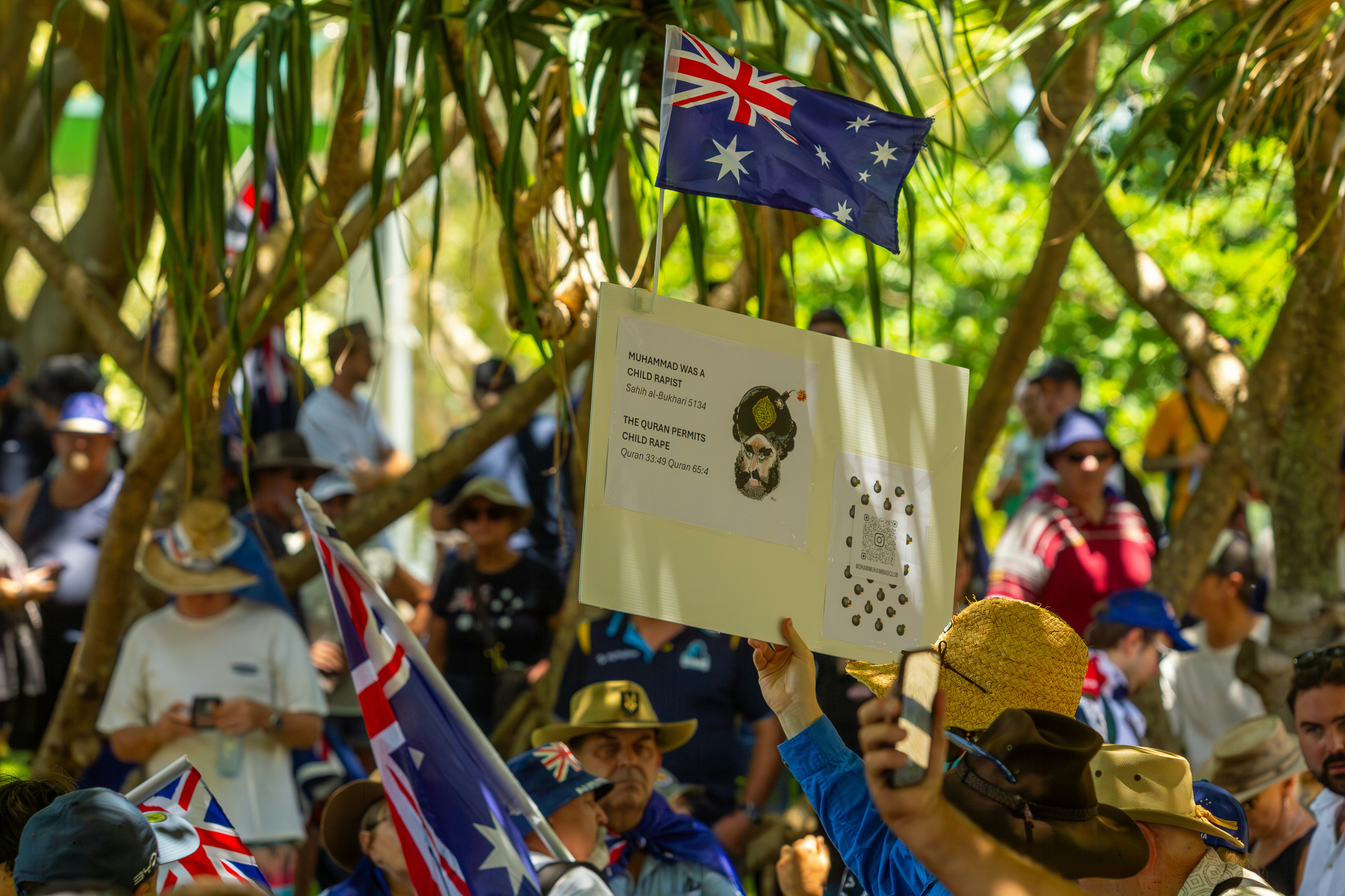 People gathered under trees with australian flags.