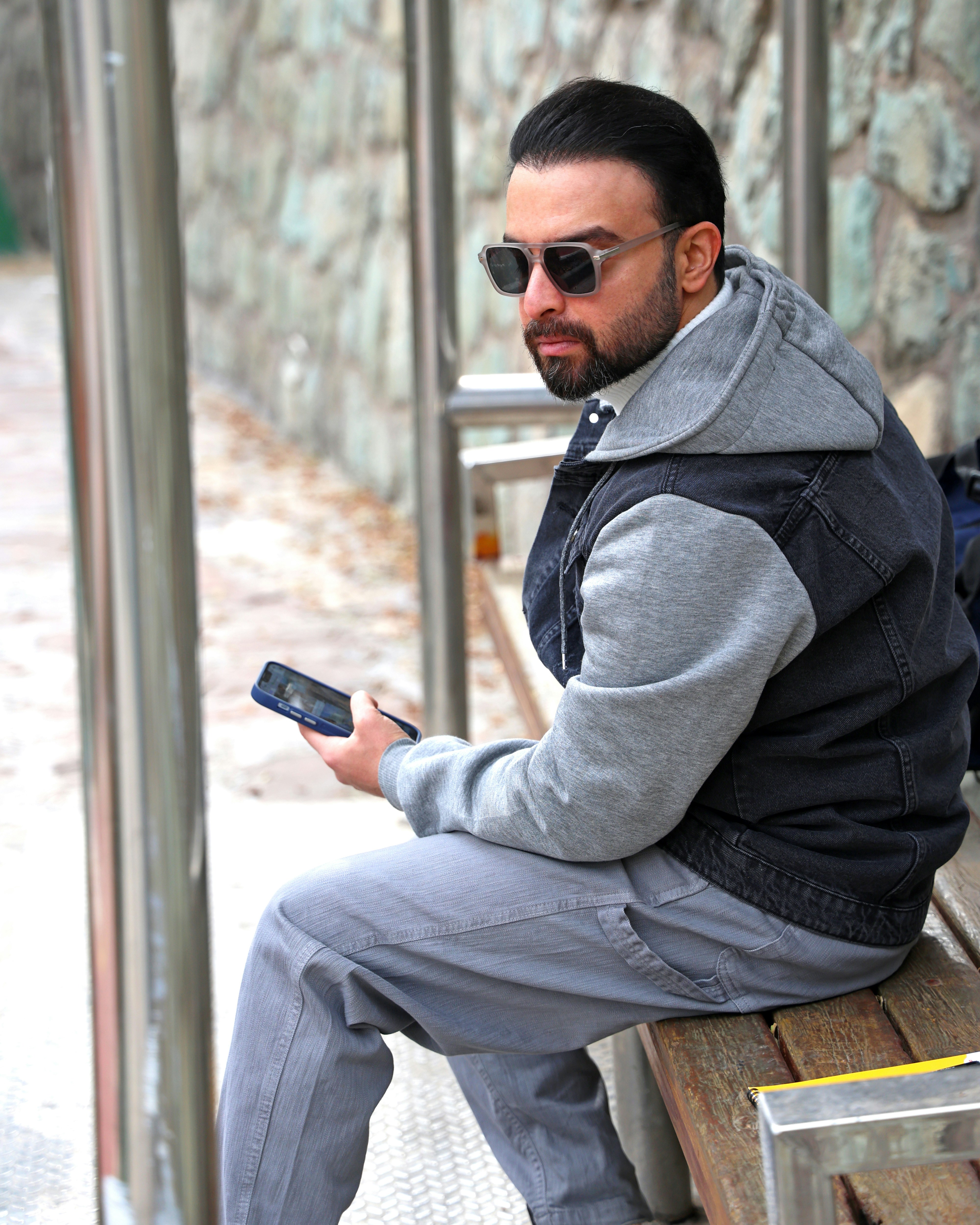 Man in sunglasses holding a smartphone on a bench.