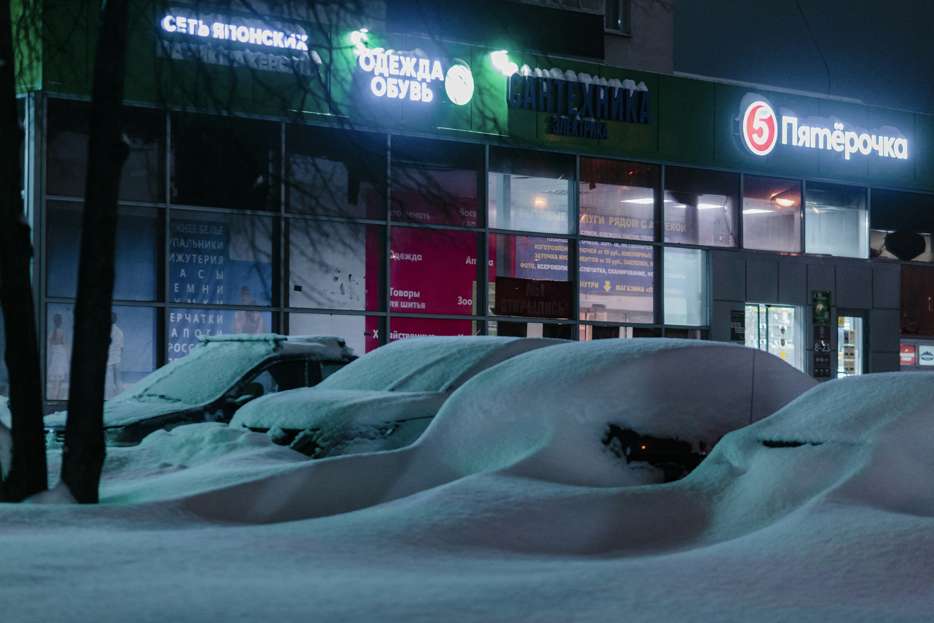 Cars parked in snow outside a brightly lit store