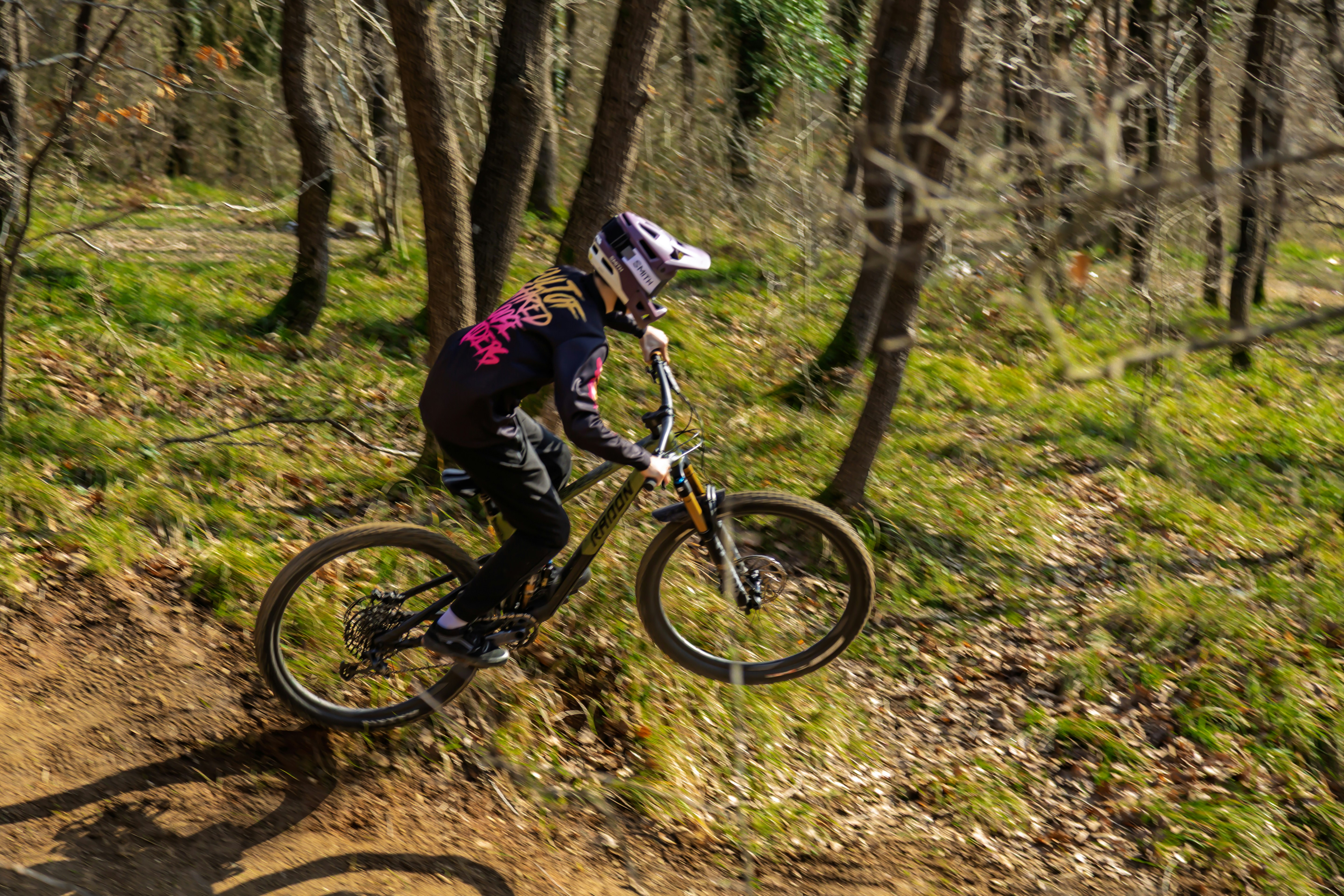 A person on a bicycle jumps over a dirt ramp.