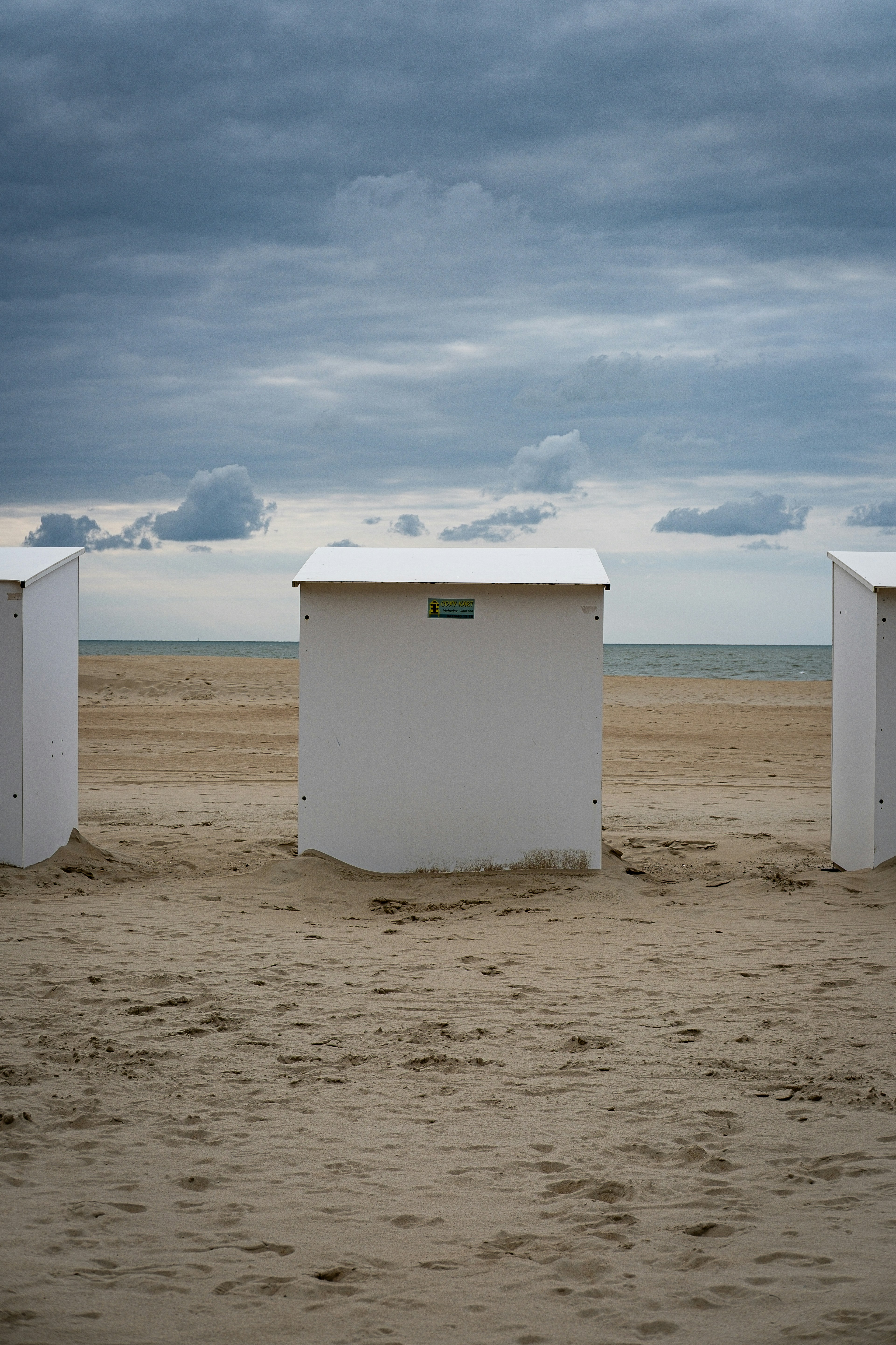 Three white beach huts on a sandy shore