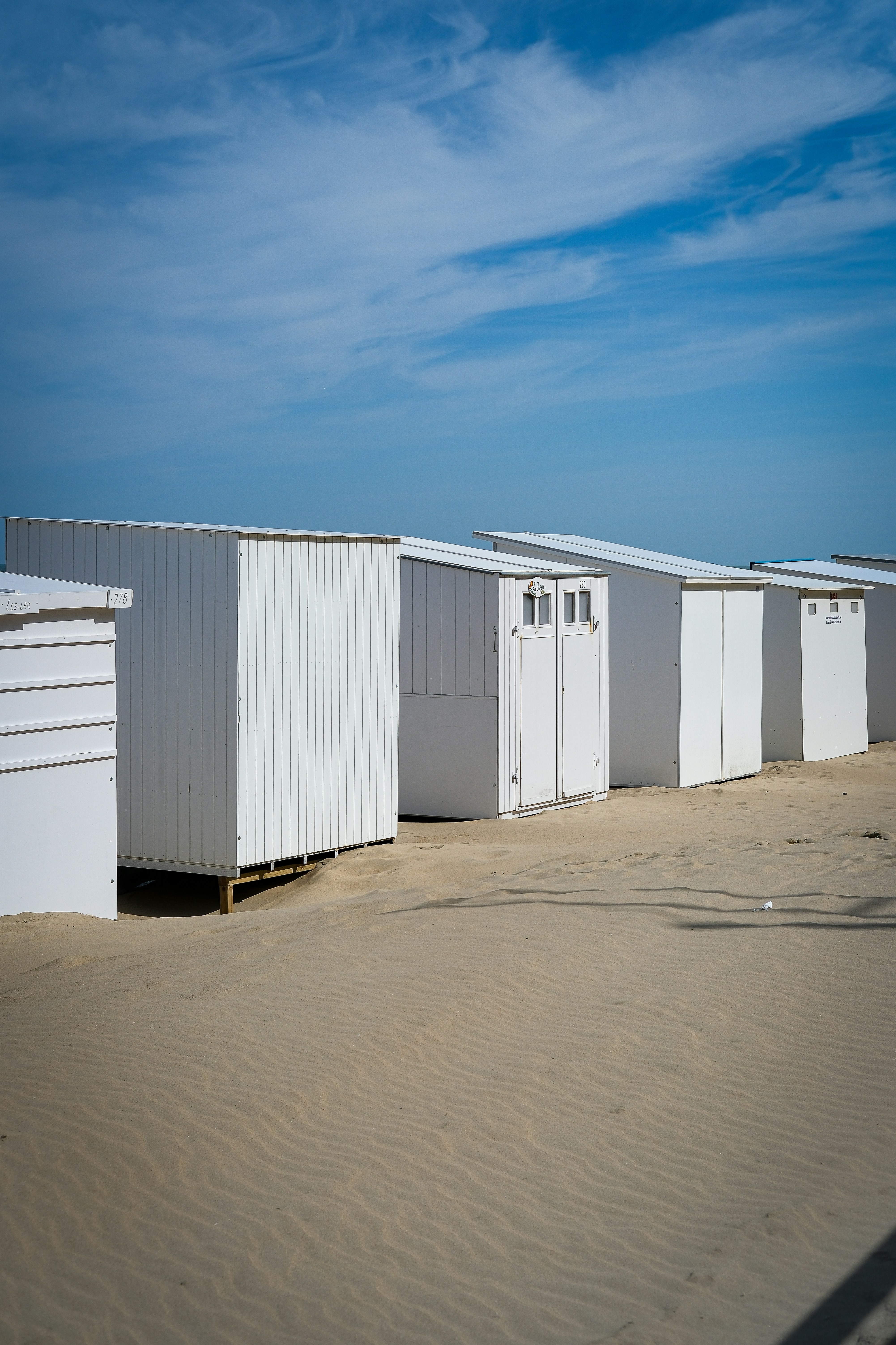 White beach huts lined up on a sandy shore.