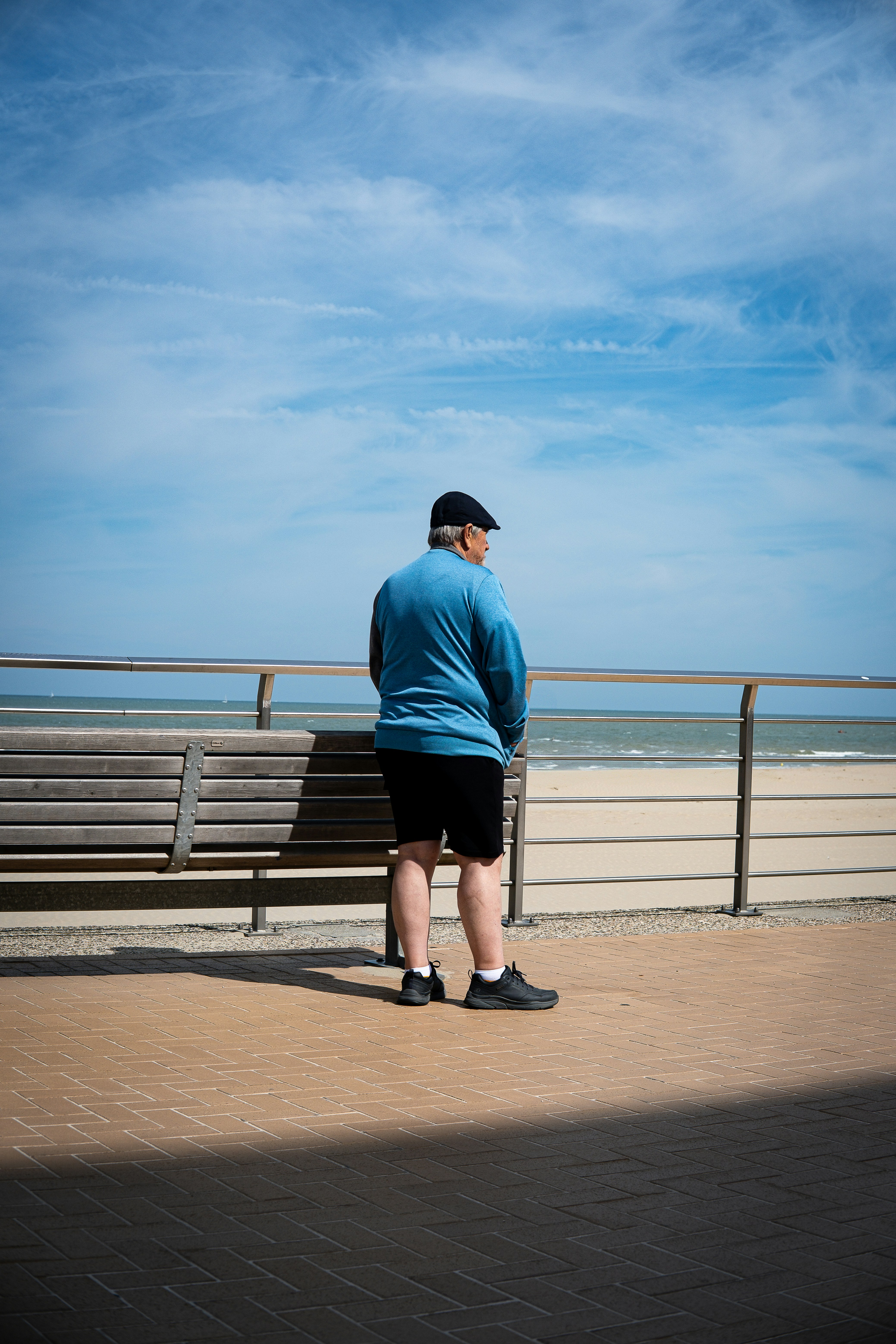 Man in blue sweatshirt stands by the ocean boardwalk.