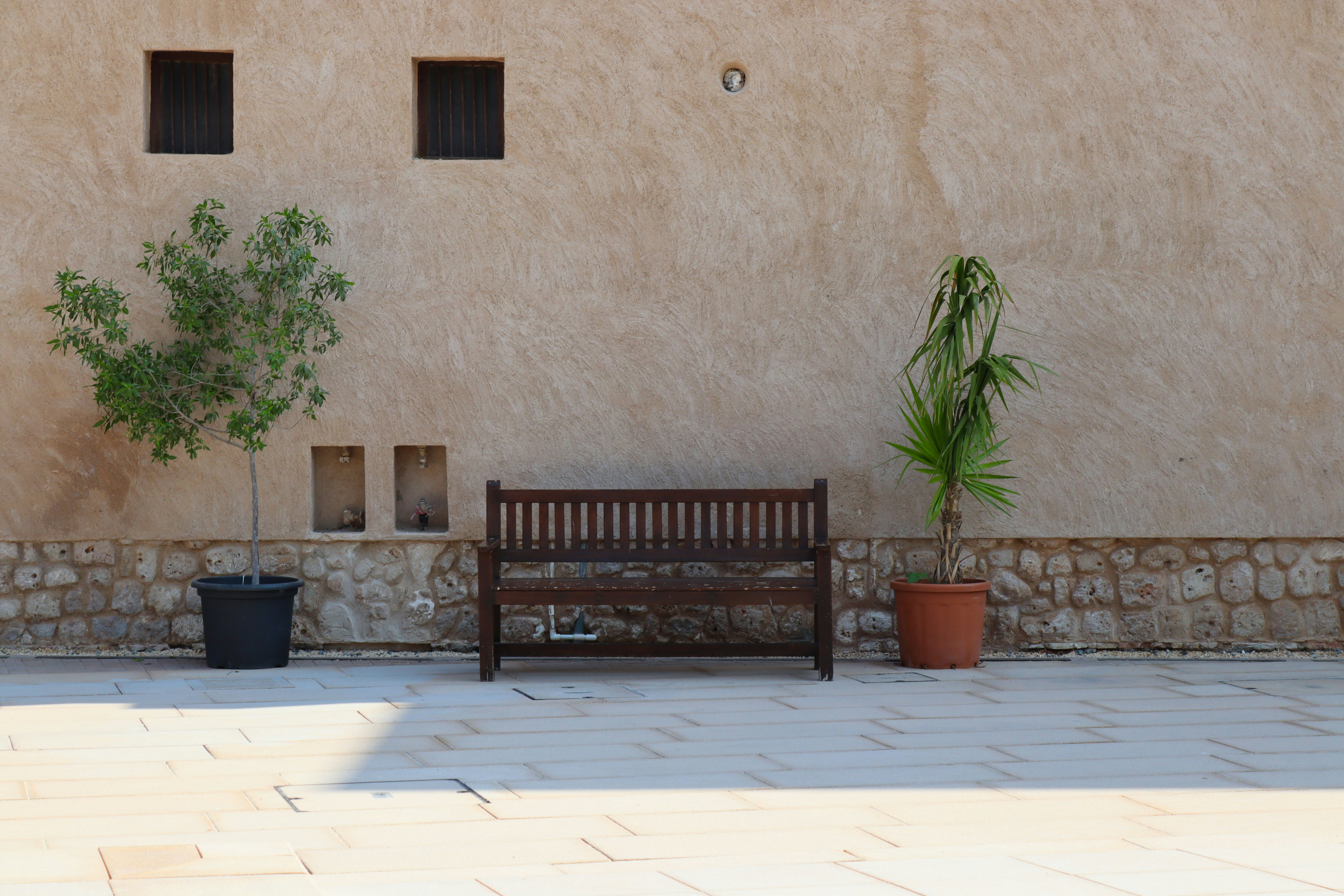 A wooden bench sits between two potted plants.