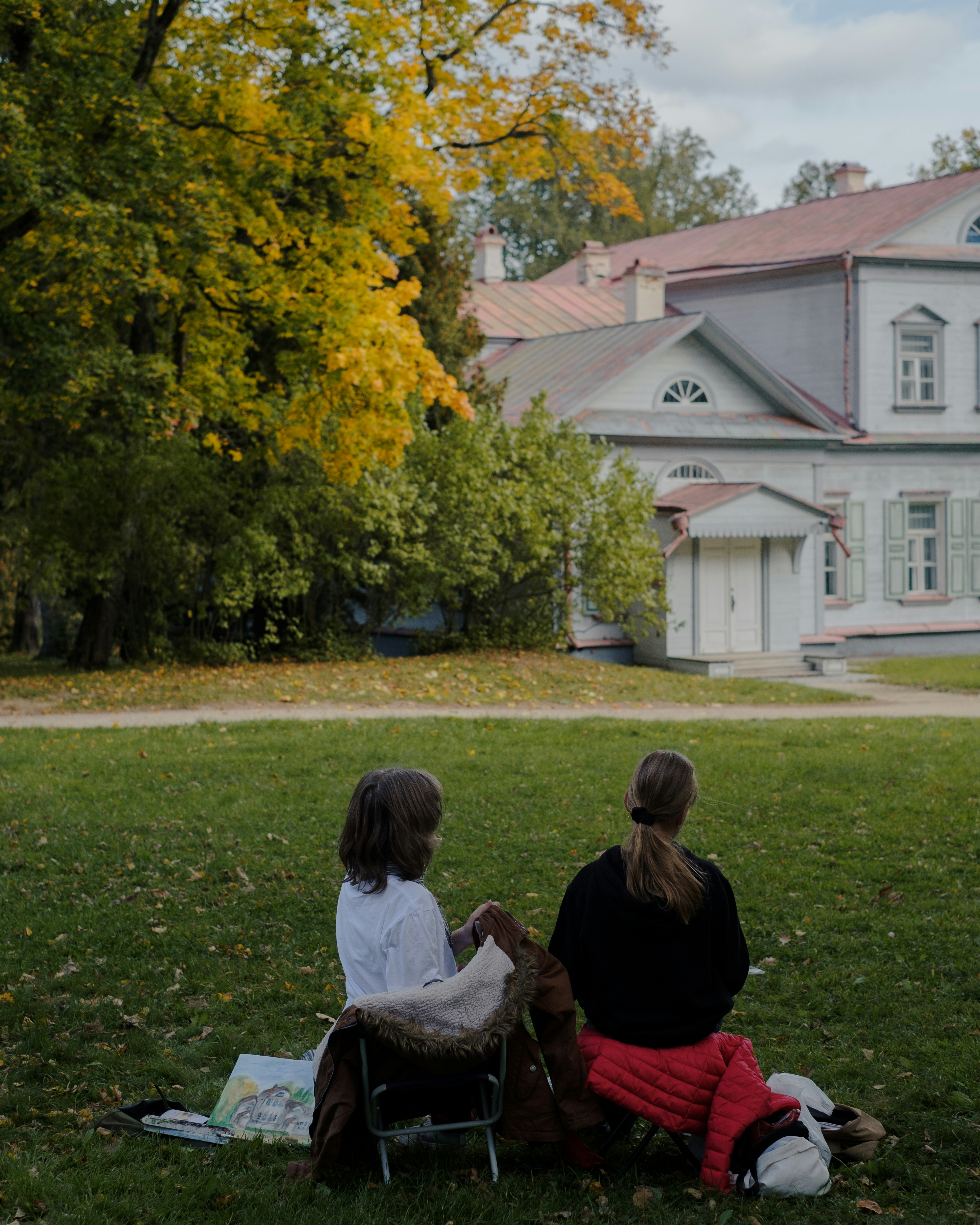 Two people sit on grass near a large building.