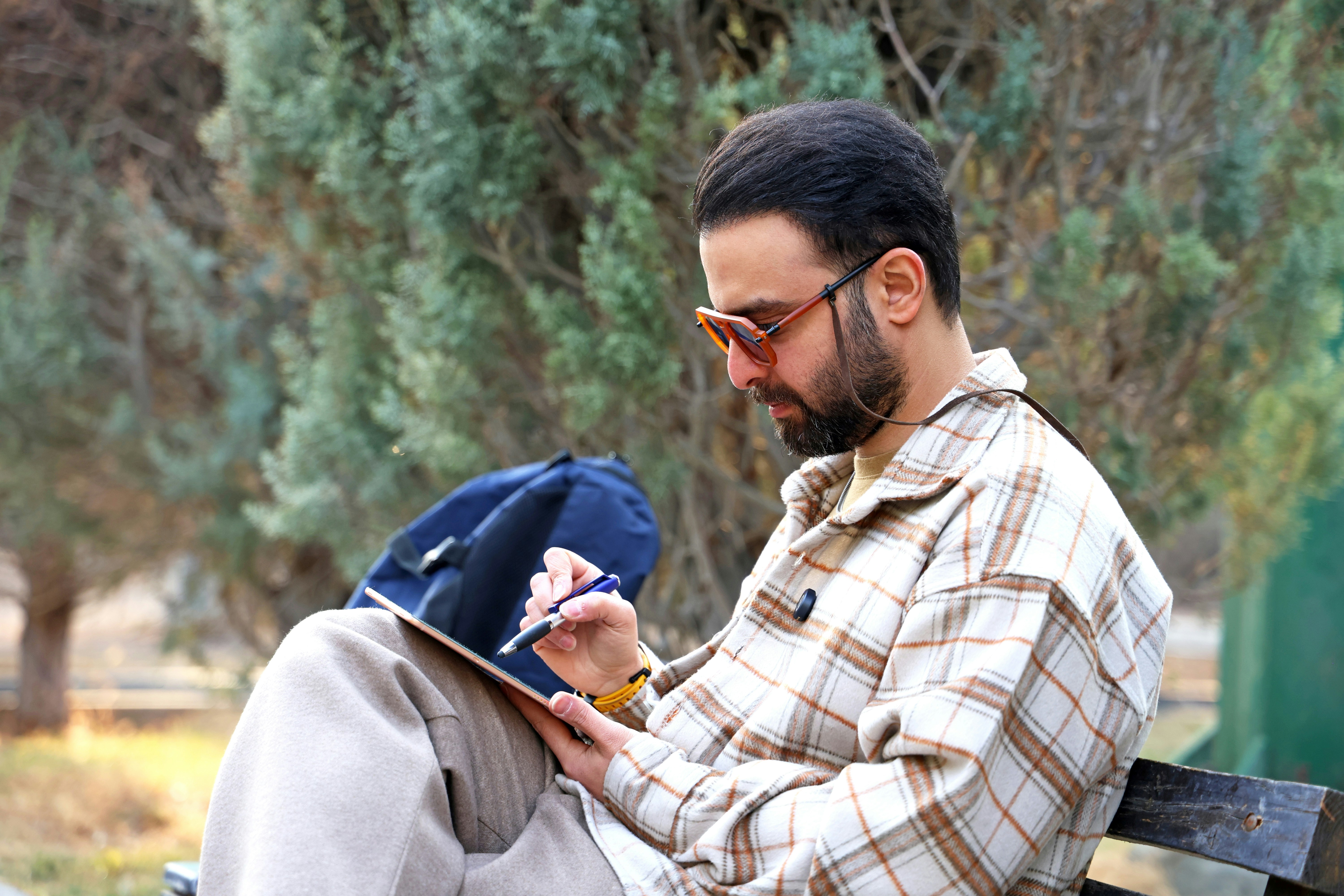 Hombre sentado en un banco, escribiendo en una tableta.