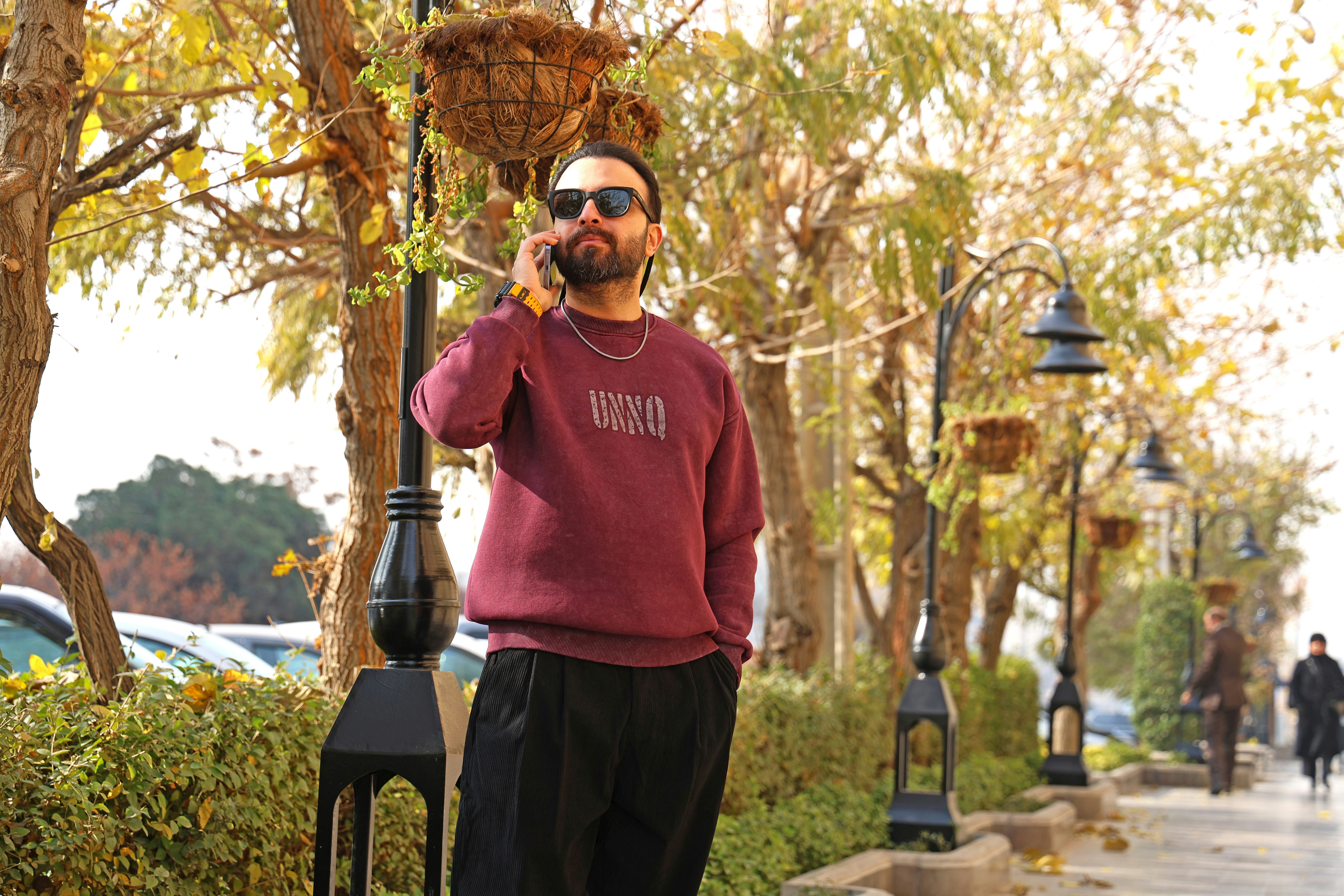 Man in maroon sweatshirt talking on phone outdoors phone outdoors.