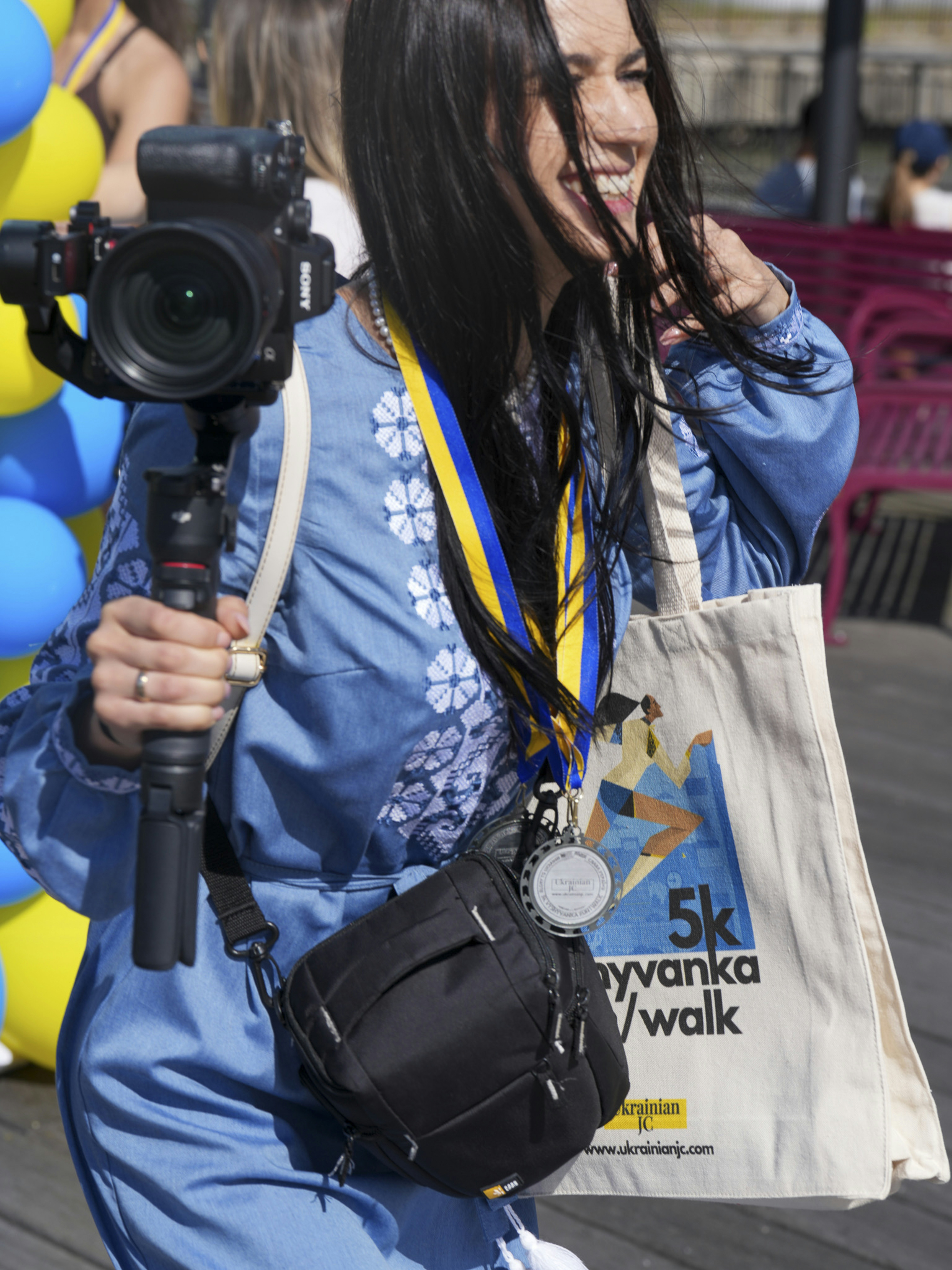 Woman in blue embroidered shirt holding camera equipment