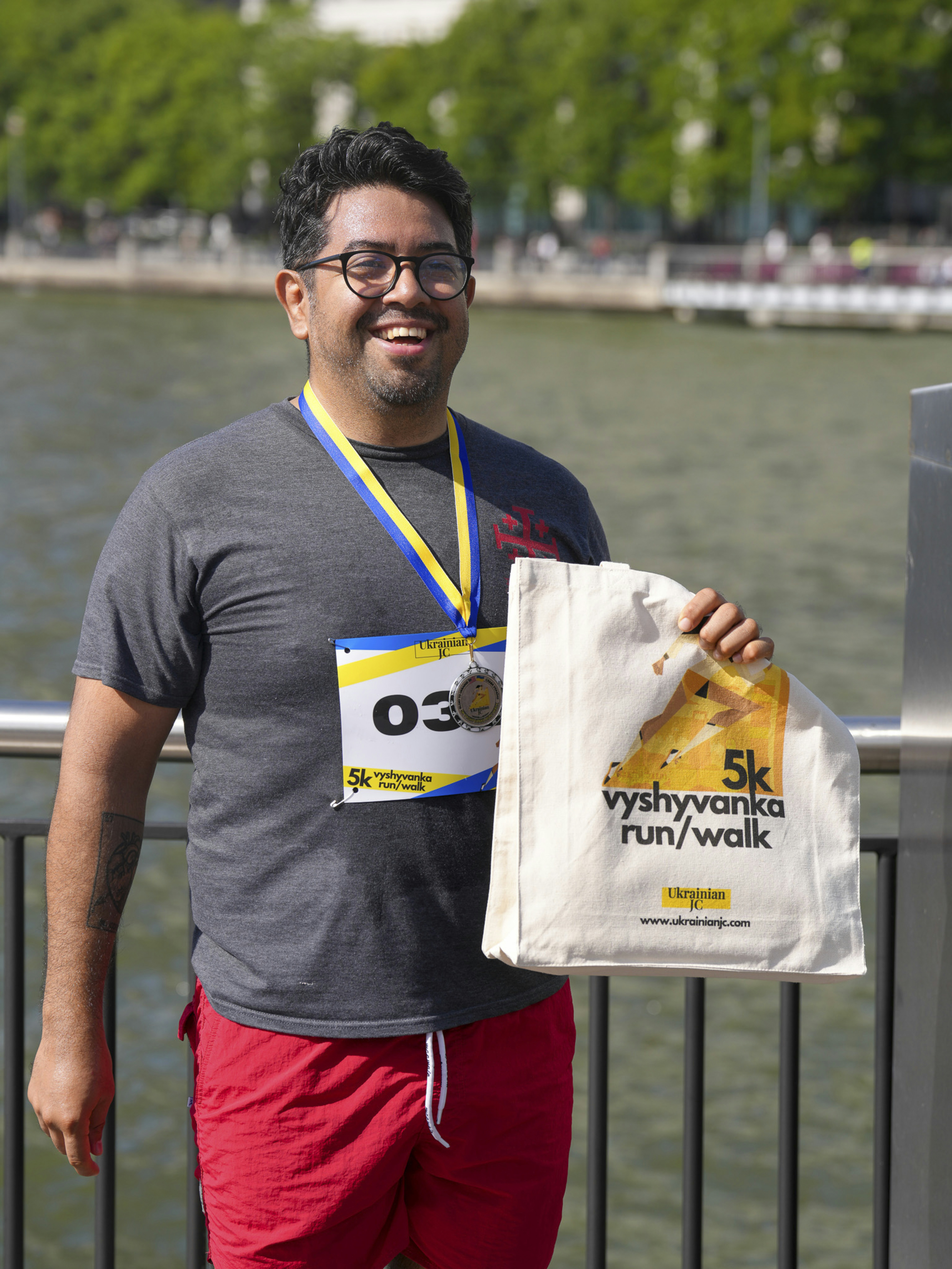 Man wearing race bib and medal holding a tote bag