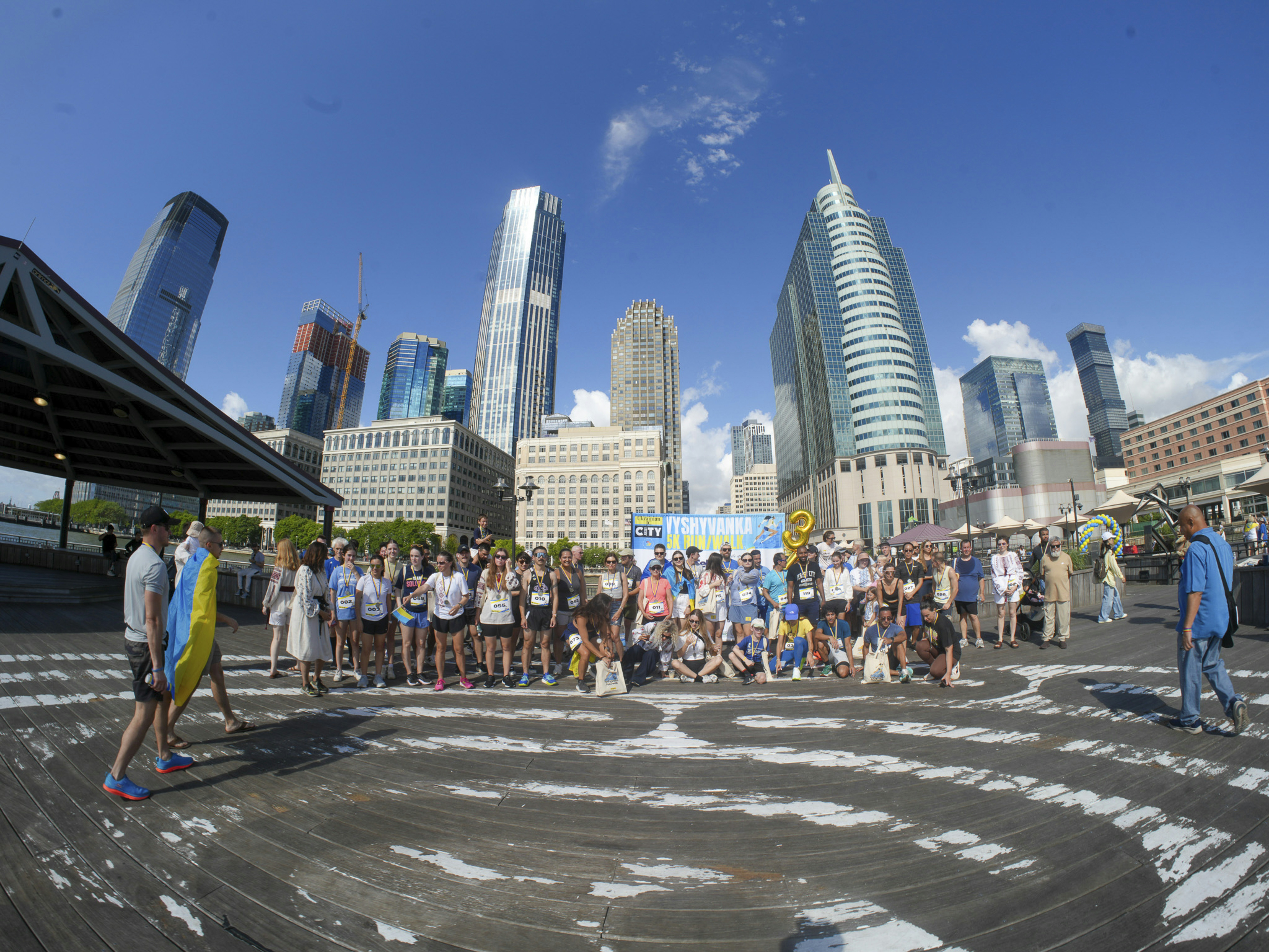 By Oleksandr Buzunov. Instagram: @buzunov.photoart A community comes together on the Jersey City waterfront for the Vyshyvanka Run, a cultural charity race celebrating Ukrainian heritage, unity, and resilience. Runners cross the finish line wearing traditional embroidered vyshyvankas alongside modern athletic gear, symbolizing the connection between history and contemporary life. Blue and yellow medals mark moments of pride, relief, and shared emotion. These candid moments capture how Ukrainian traditions live on within the diaspora, carried forward through movement, community.