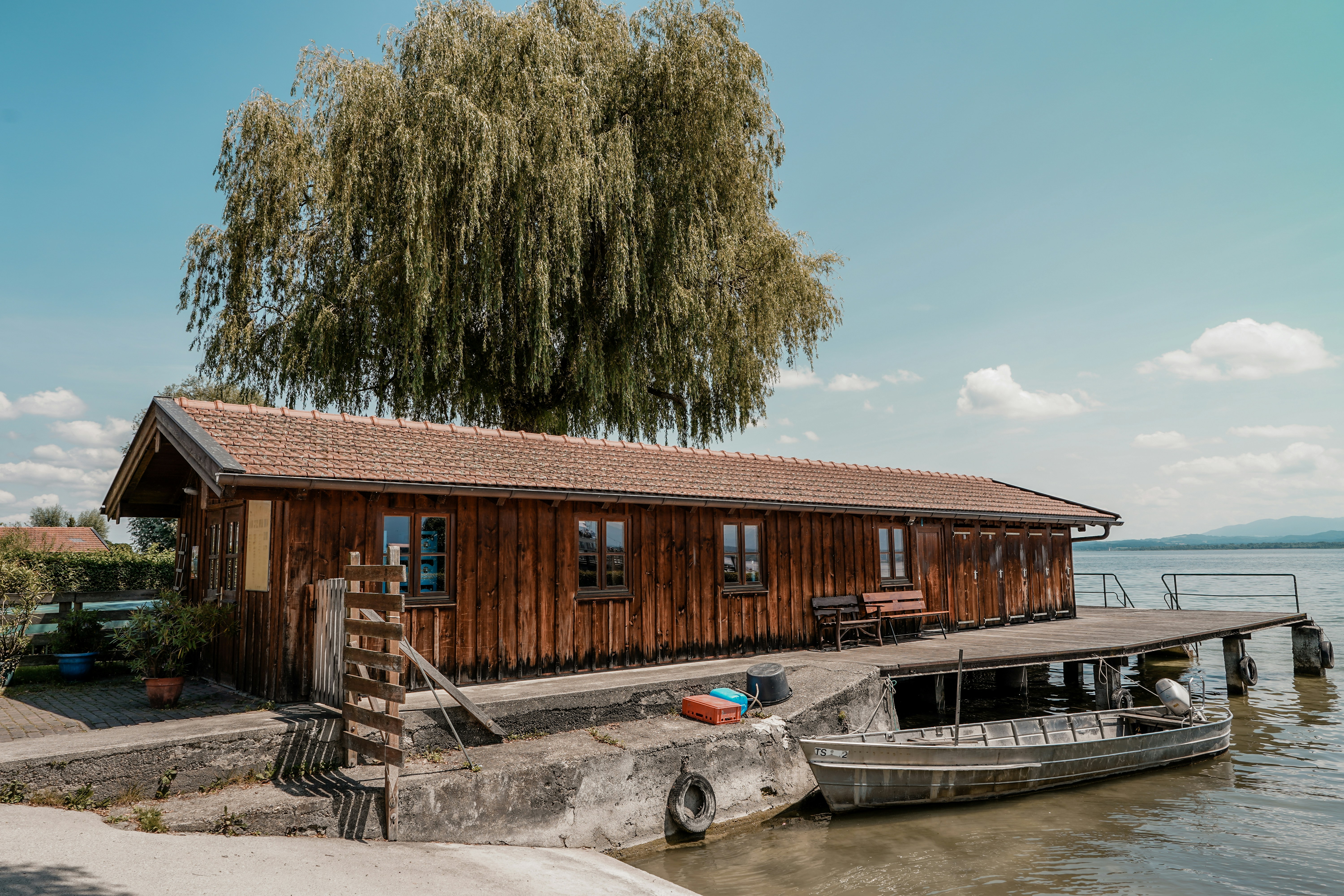 Wooden boathouse with a weeping willow tree and boat.