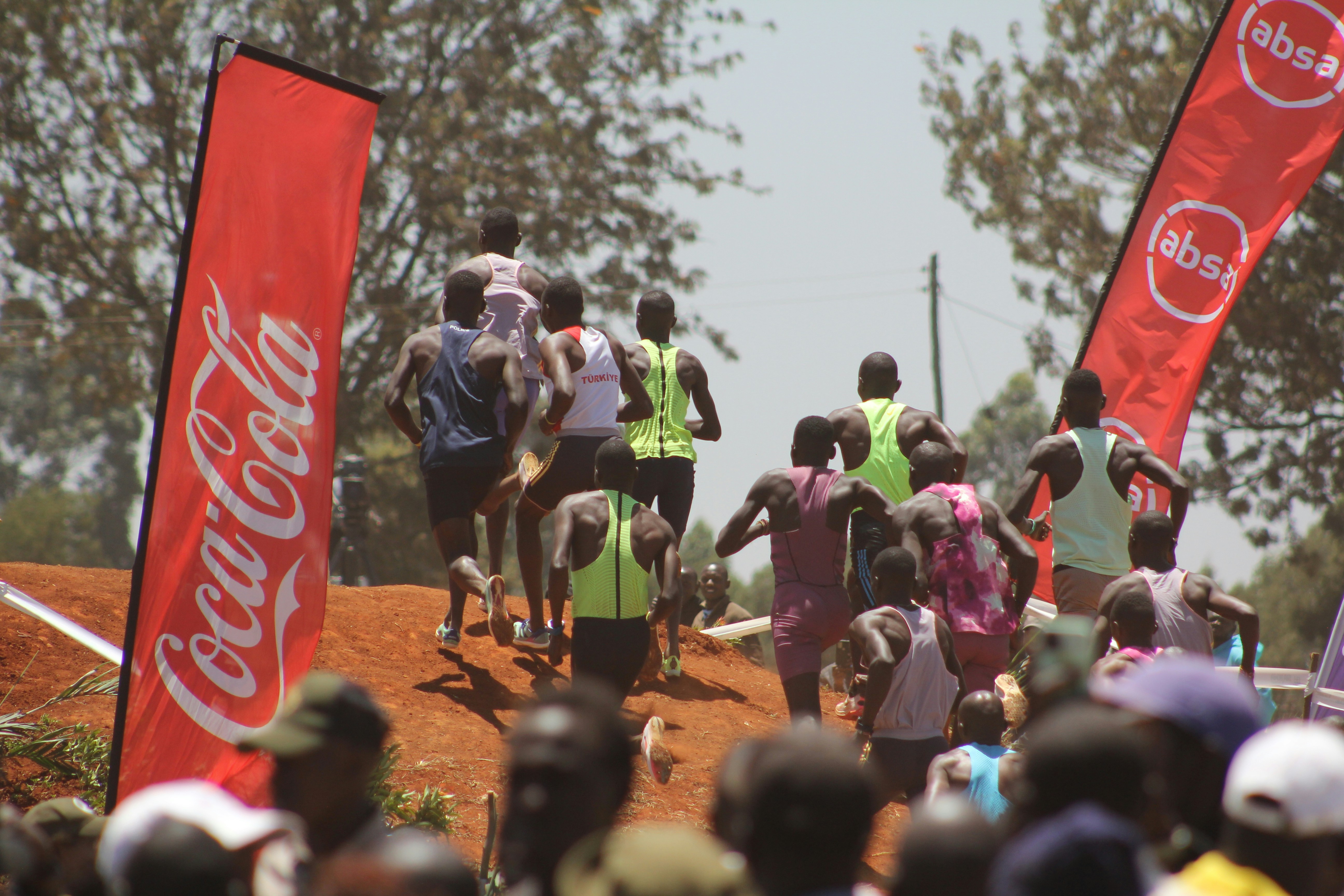 Runners ascend a dirt hill between coca-cola banners.