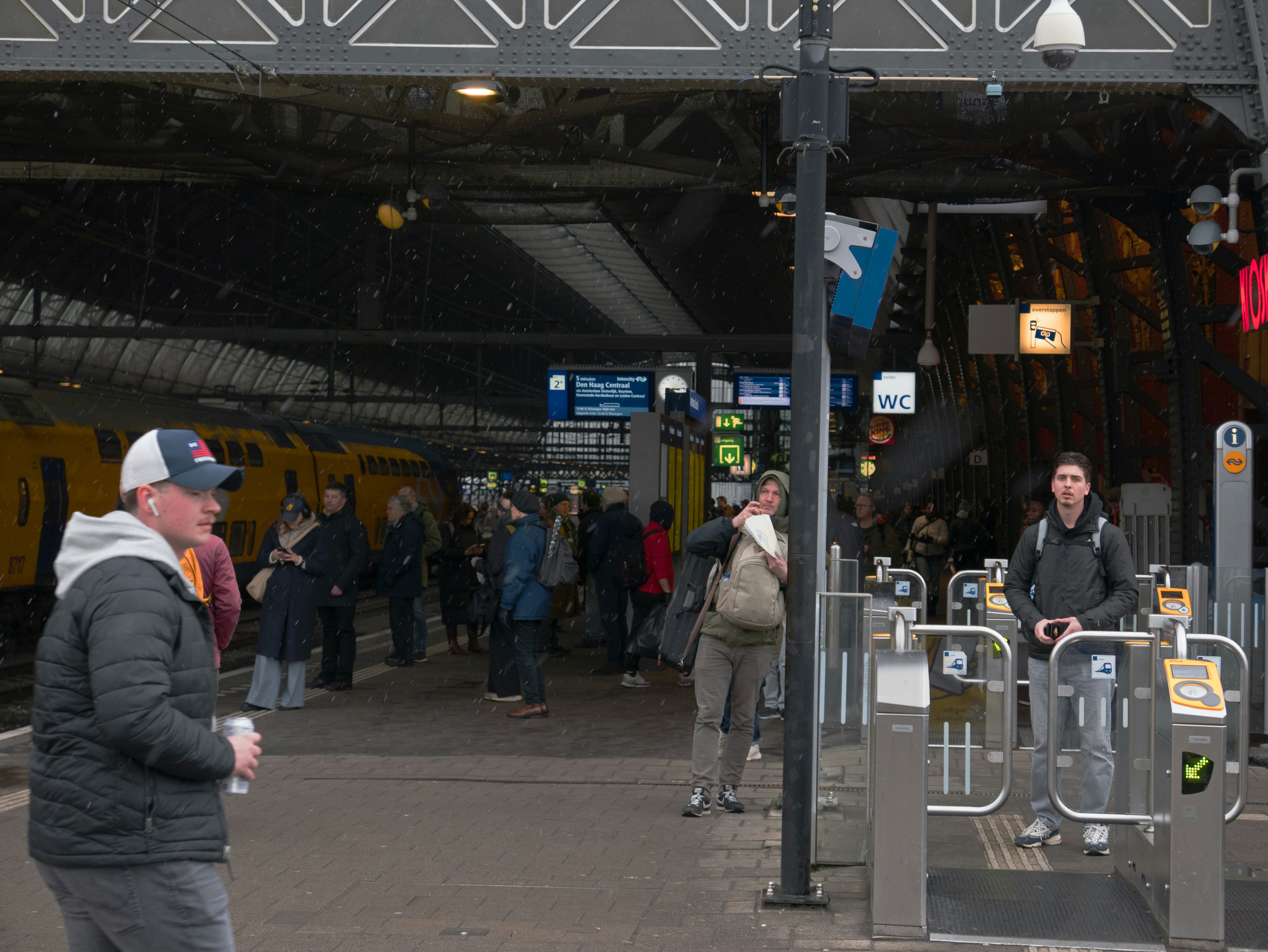 People waiting at a train station entrance with turnstiles.