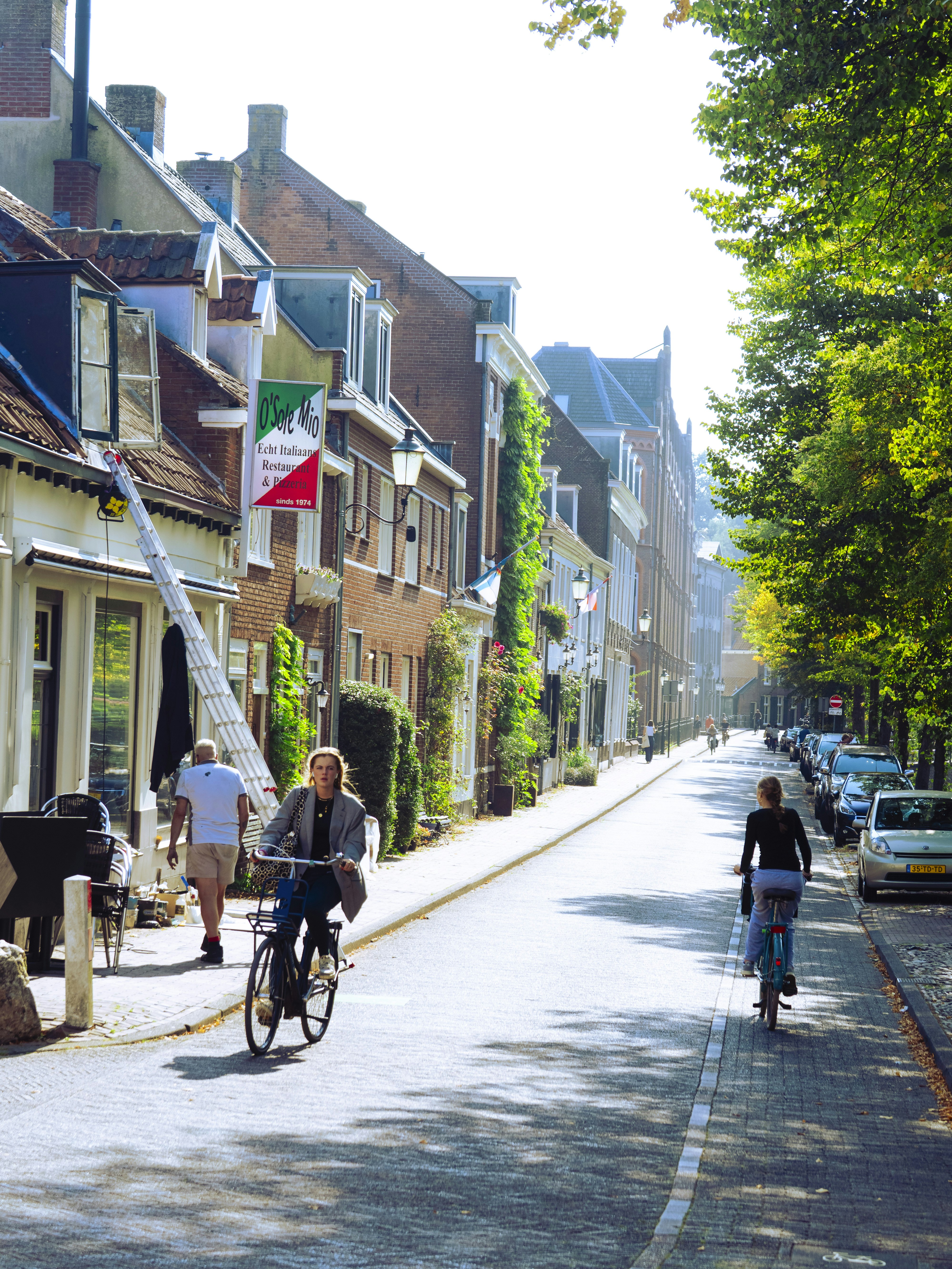 People cycling on a sunny street lined with buildings.