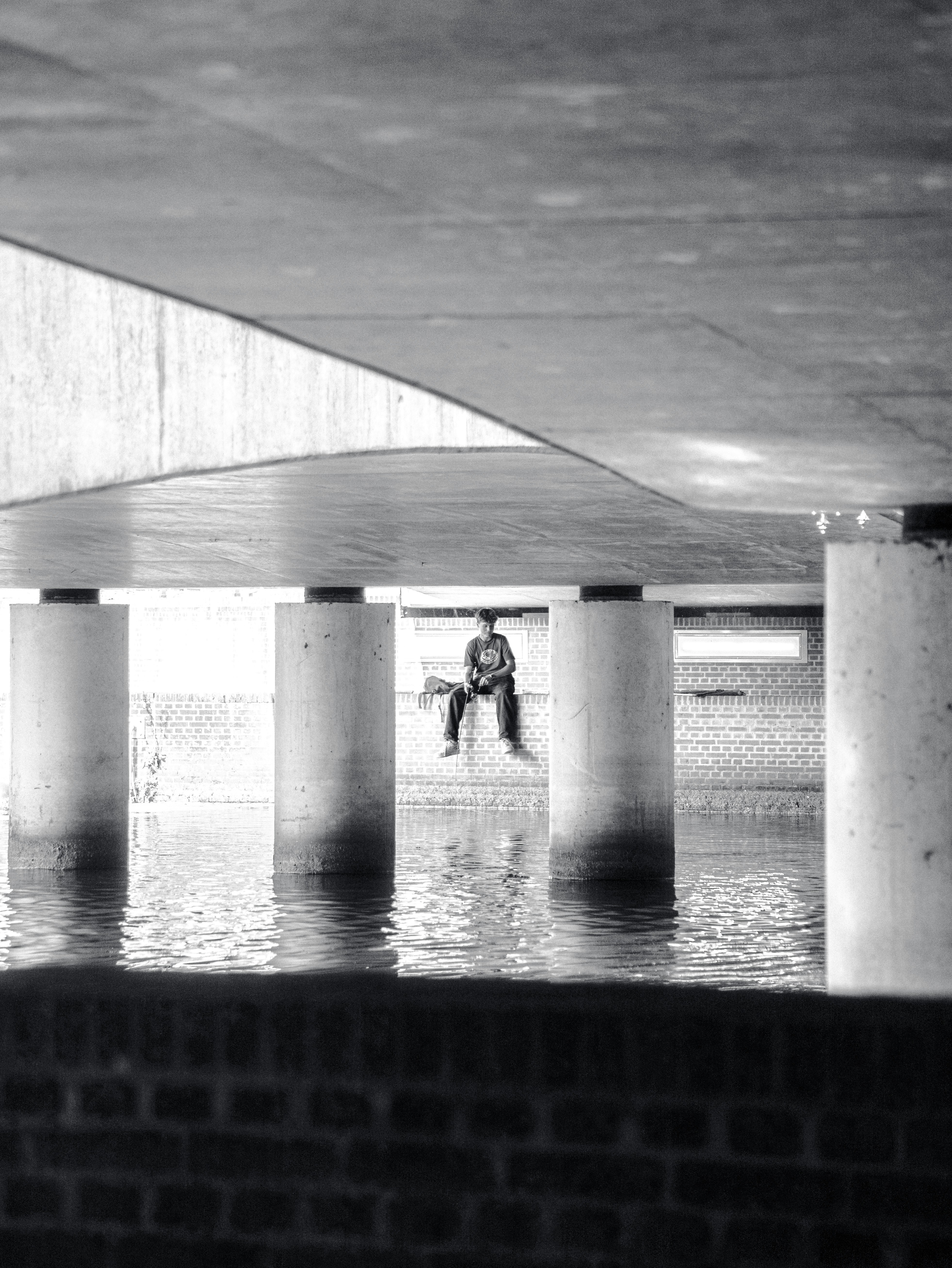 Man sitting under a concrete bridge by water
