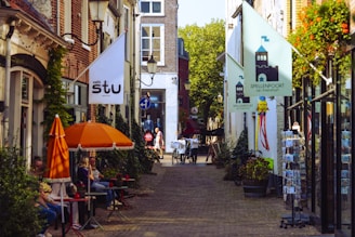 People sitting at outdoor cafe tables on a sunny street.