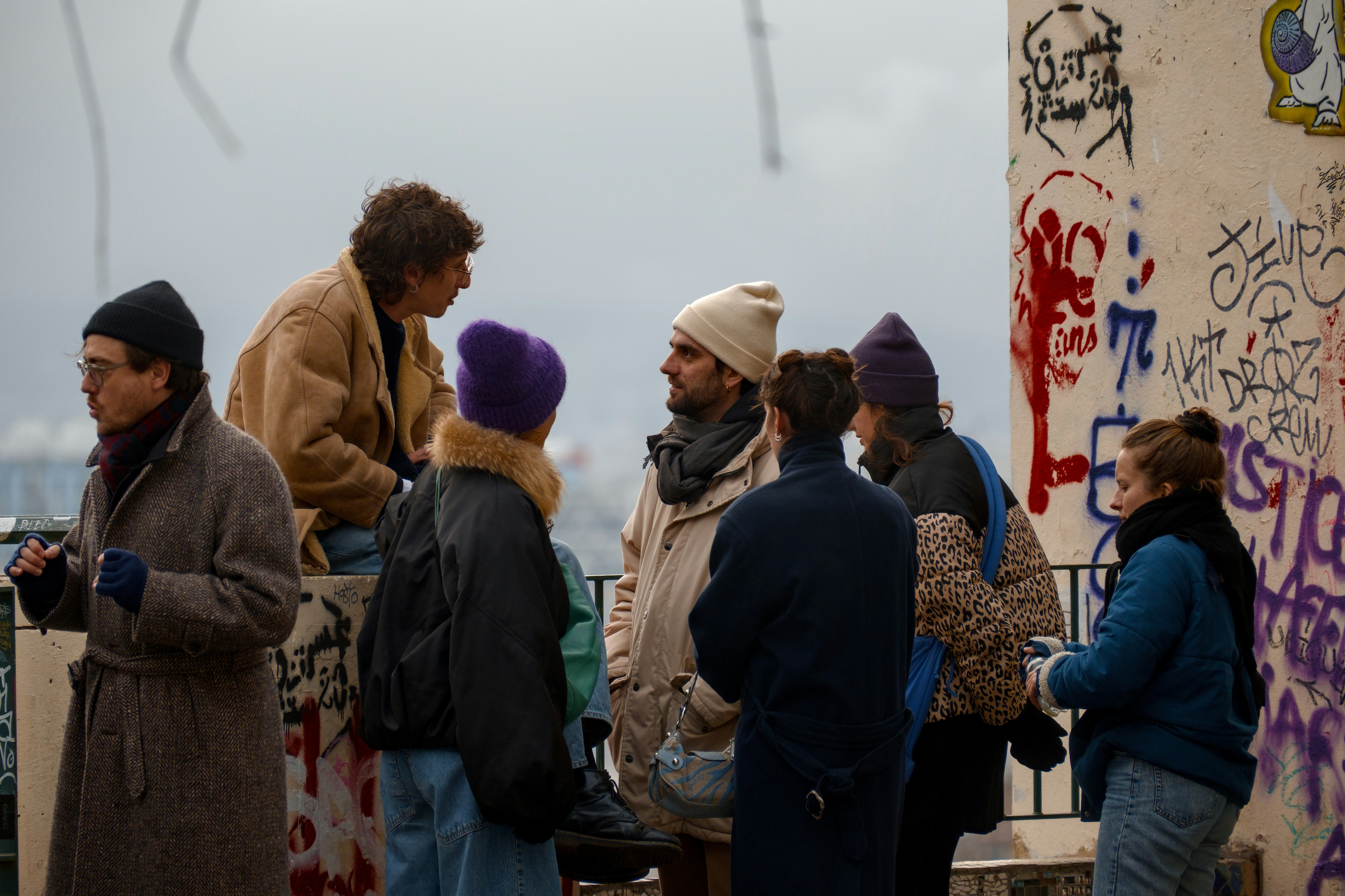 A group of people gathered outdoors near graffiti-covered wall