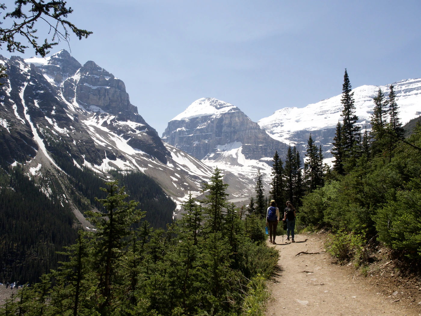 Two hikers walking beneath dramatic snow-streaked mountain peaks